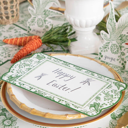A Green Regal Peacock Table Card with &quot;Happy Easter!&quot; written on it resting on the plate of an elegant place setting.