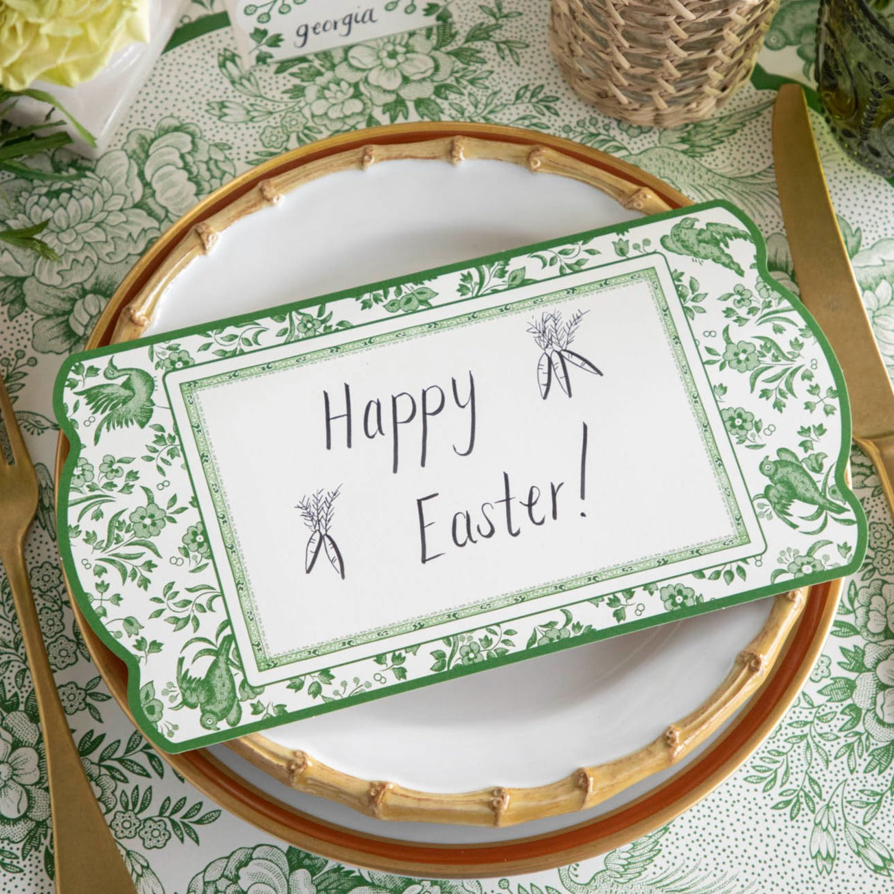 A Green Regal Peacock Table Card with &quot;Happy Easter!&quot; written on it resting on the plate of an elegant place setting.