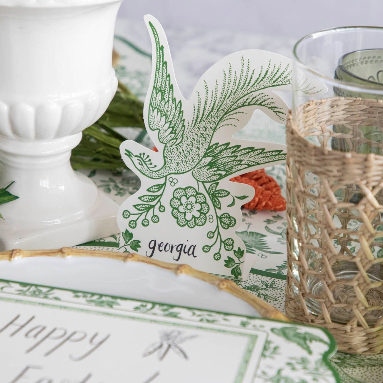 A table setting with Green Asiatic Pheasants place cards by Hester & Cook, green and white plates, a vase, and a place card to make guests feel special.