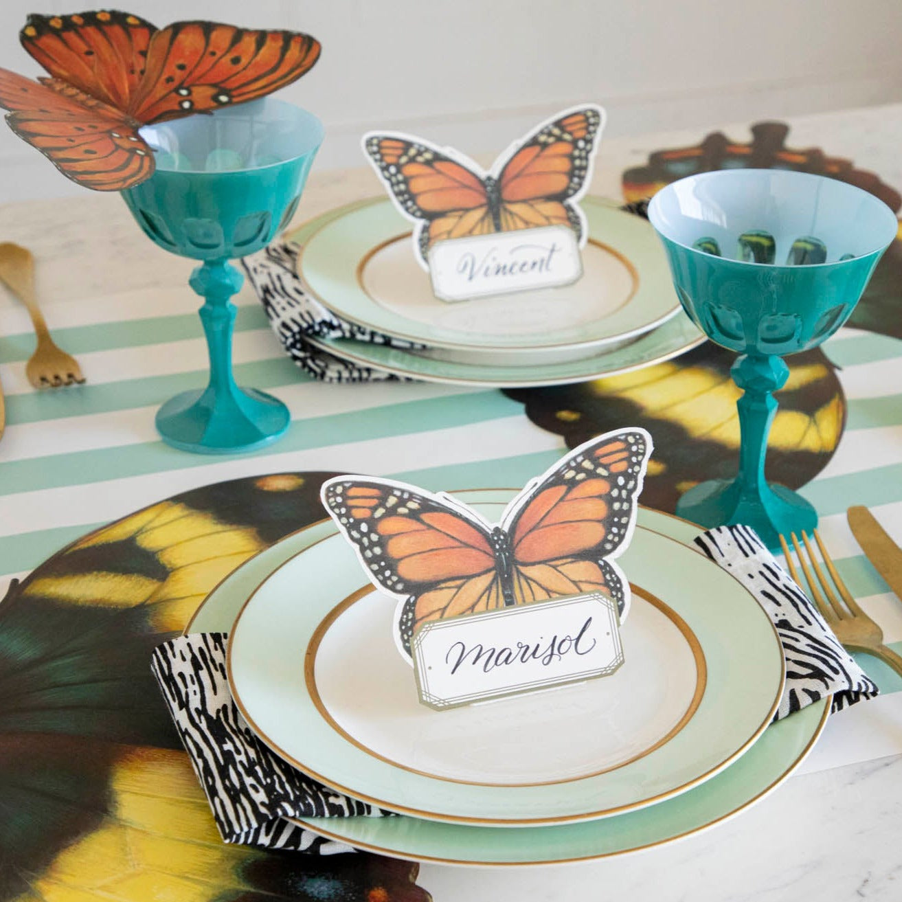 An elegant butterfly-themed table setting featuring an orange Butterfly Table Card resting on a wine glass. 