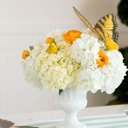 A view from the side of two Butterfly Table Accents, one on the table and one on a bouquet of white flowers, showing how folding the wings up slightly creates a realistic butterfly effect.