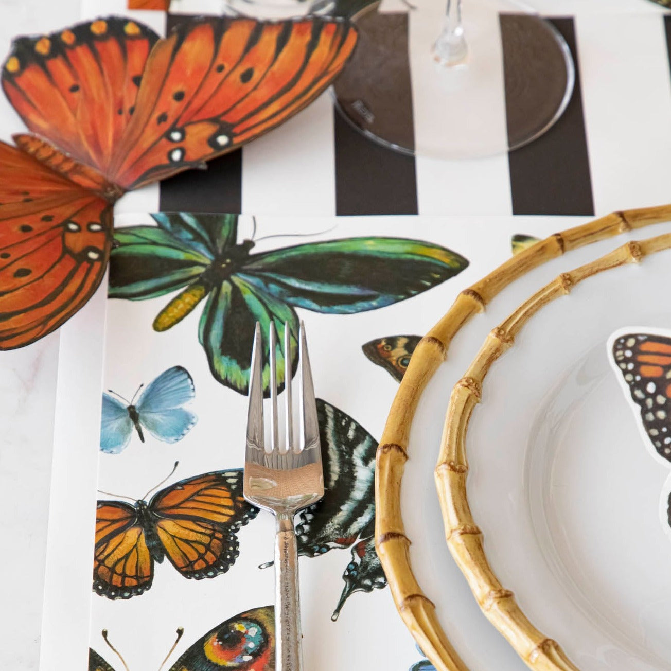 Close-up of an elegant place setting, with the orange Butterfly Table Accent resting near the placemat.