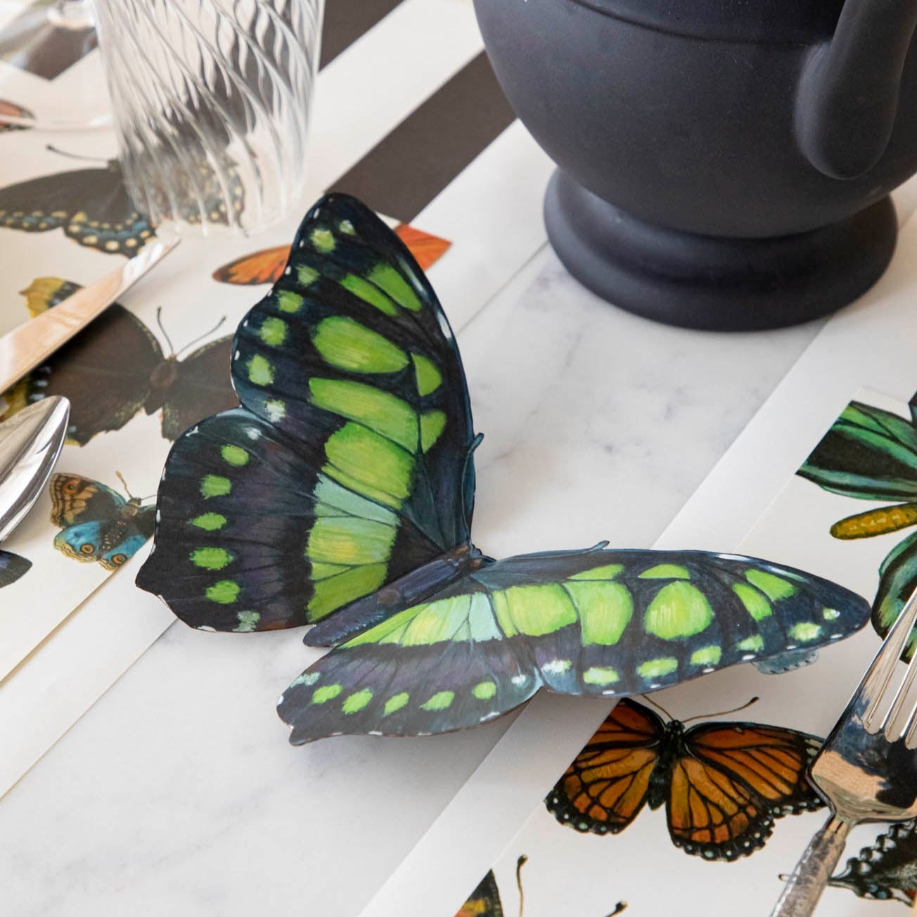 A green and black Butterfly Table Accent resting on a table between place settings.