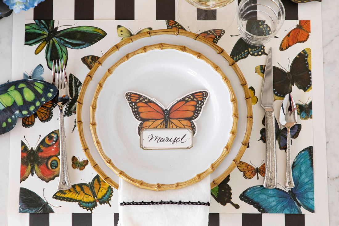 Top-down view of an elegant butterfly-themed place setting featuring a Monarch Butterfly Place Card labeled &quot;Marisol&quot; laying flat on the plate.