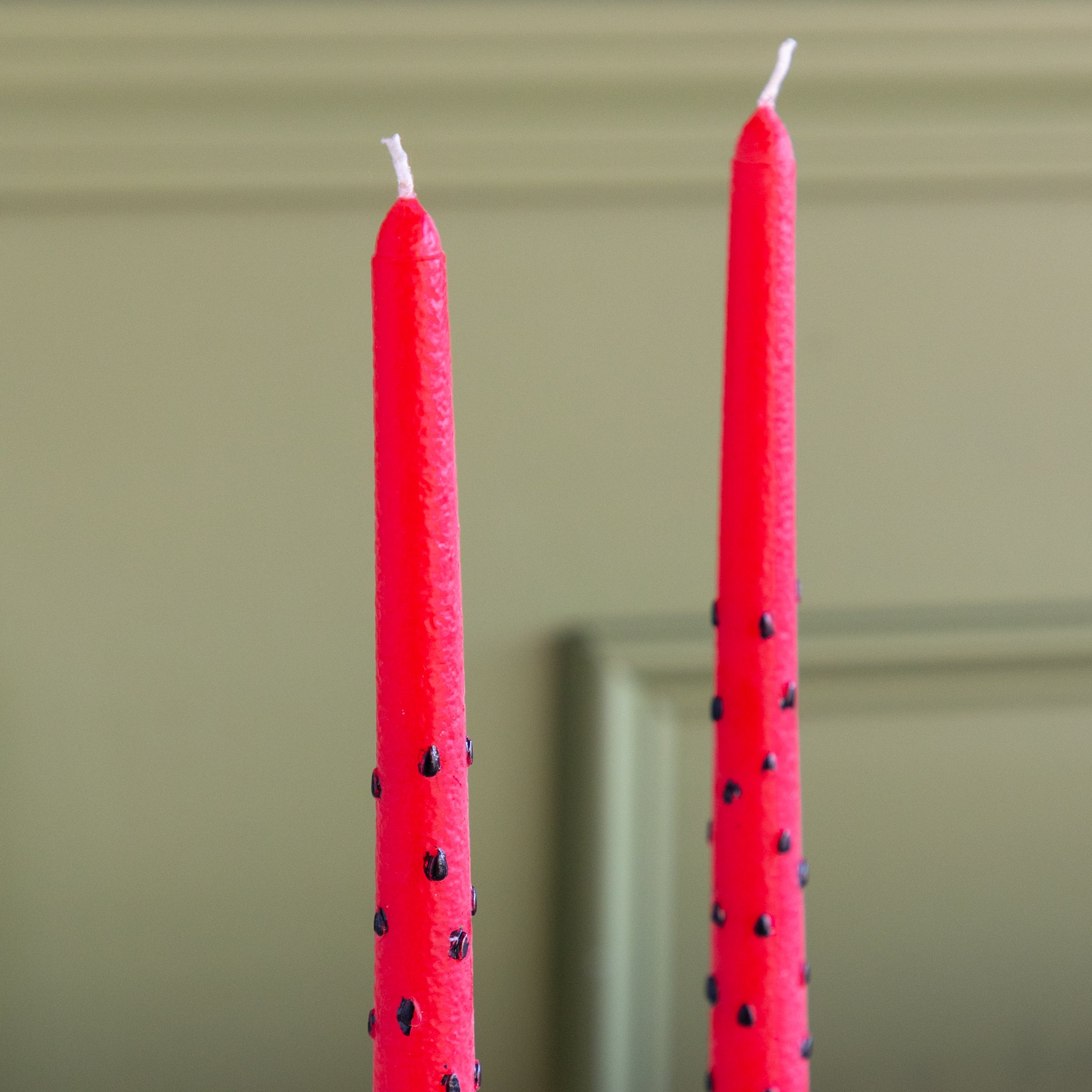 Two Watermelon Taper Candles on a green wall background.