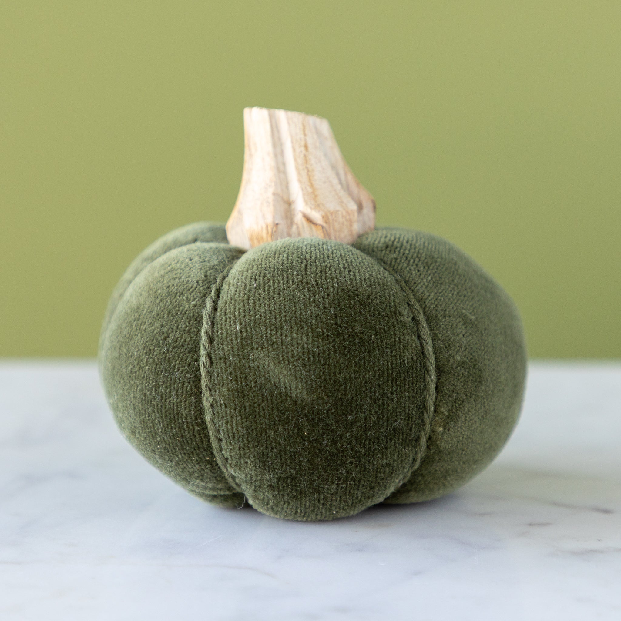 Green velvet pumpkin with a wooden stem on a marble table.