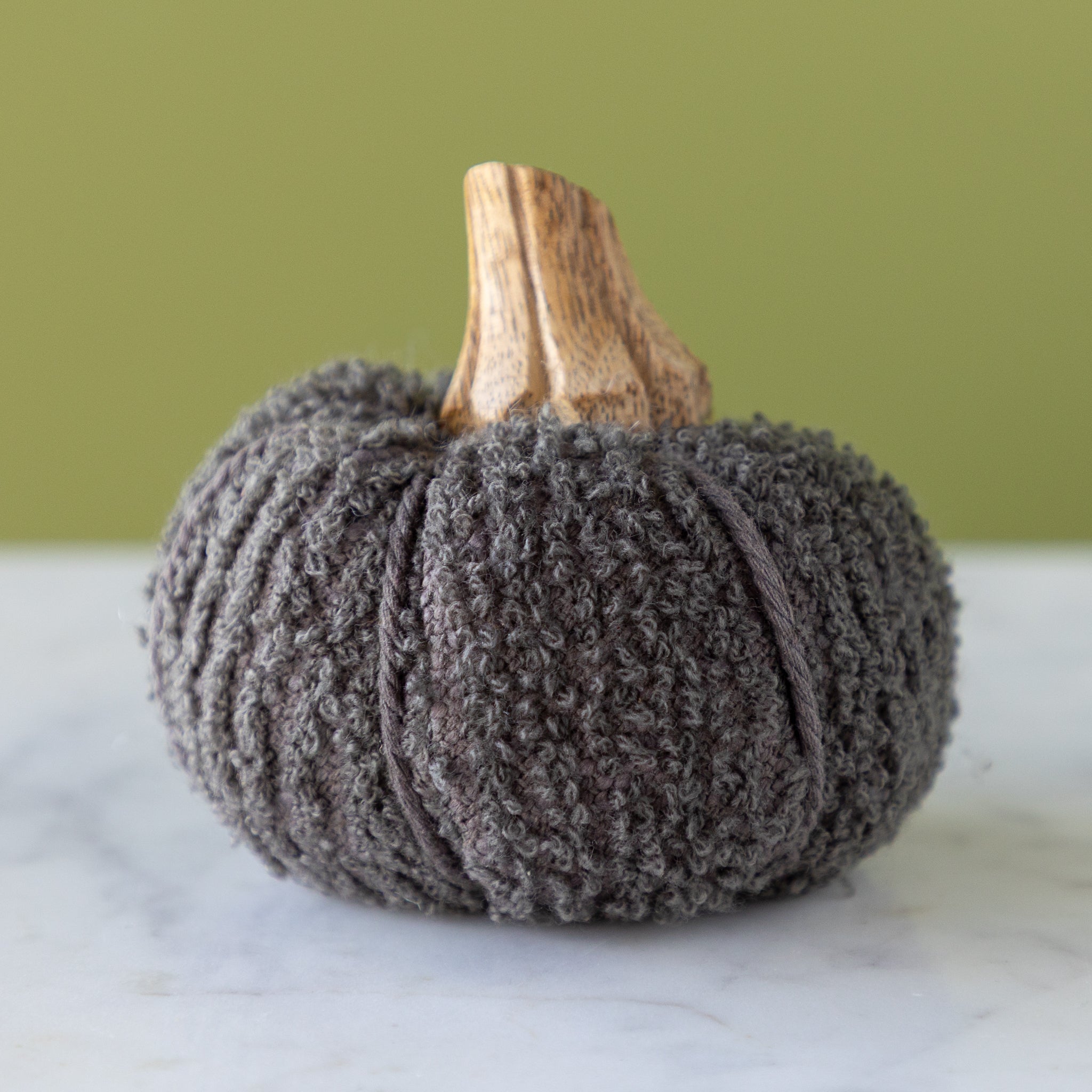 Slate bouclé pumpkin with a wooden stem on a marble table.