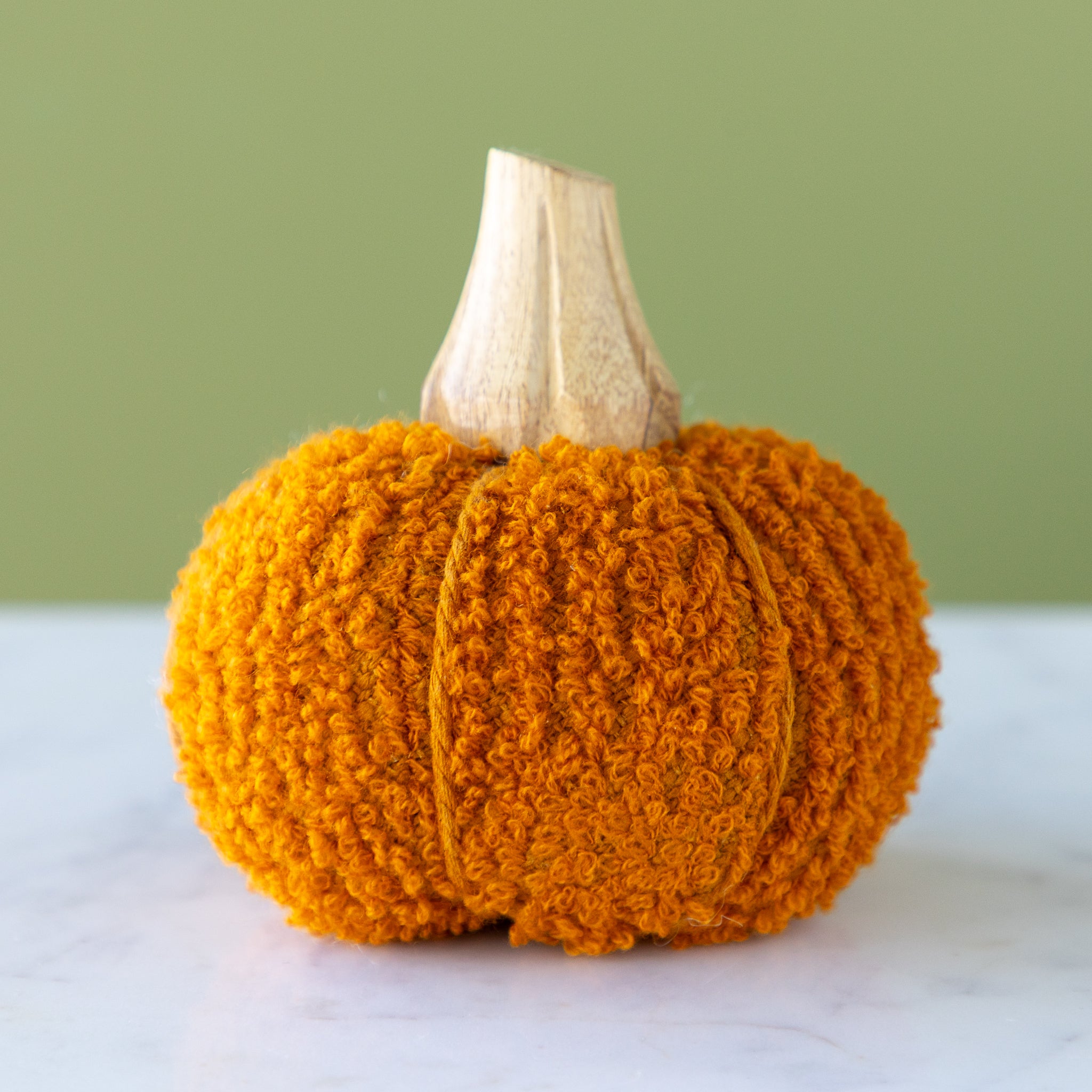 Orange bouclé pumpkin with a wooden stem on a marble table.