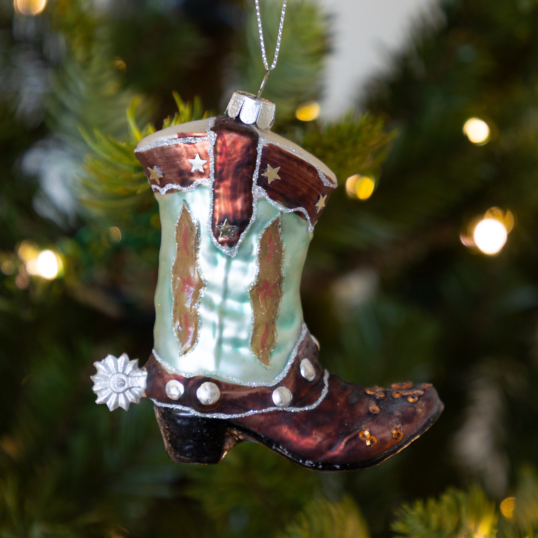 Decorative cowboy boot ornament on a Christmas tree with blurred lights in the background.