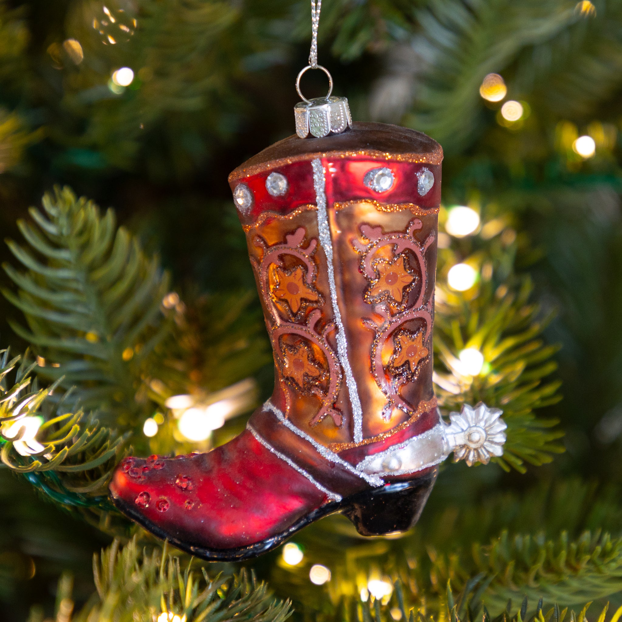 Decorative glass cowboy boot ornament on a Christmas tree with lights.