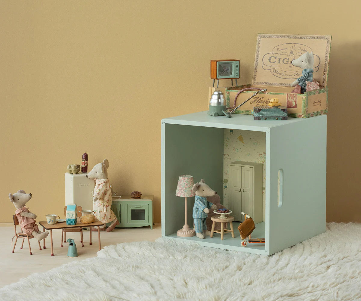 Miniature dollhouse with furniture and accessories on a soft surface against a beige wall.