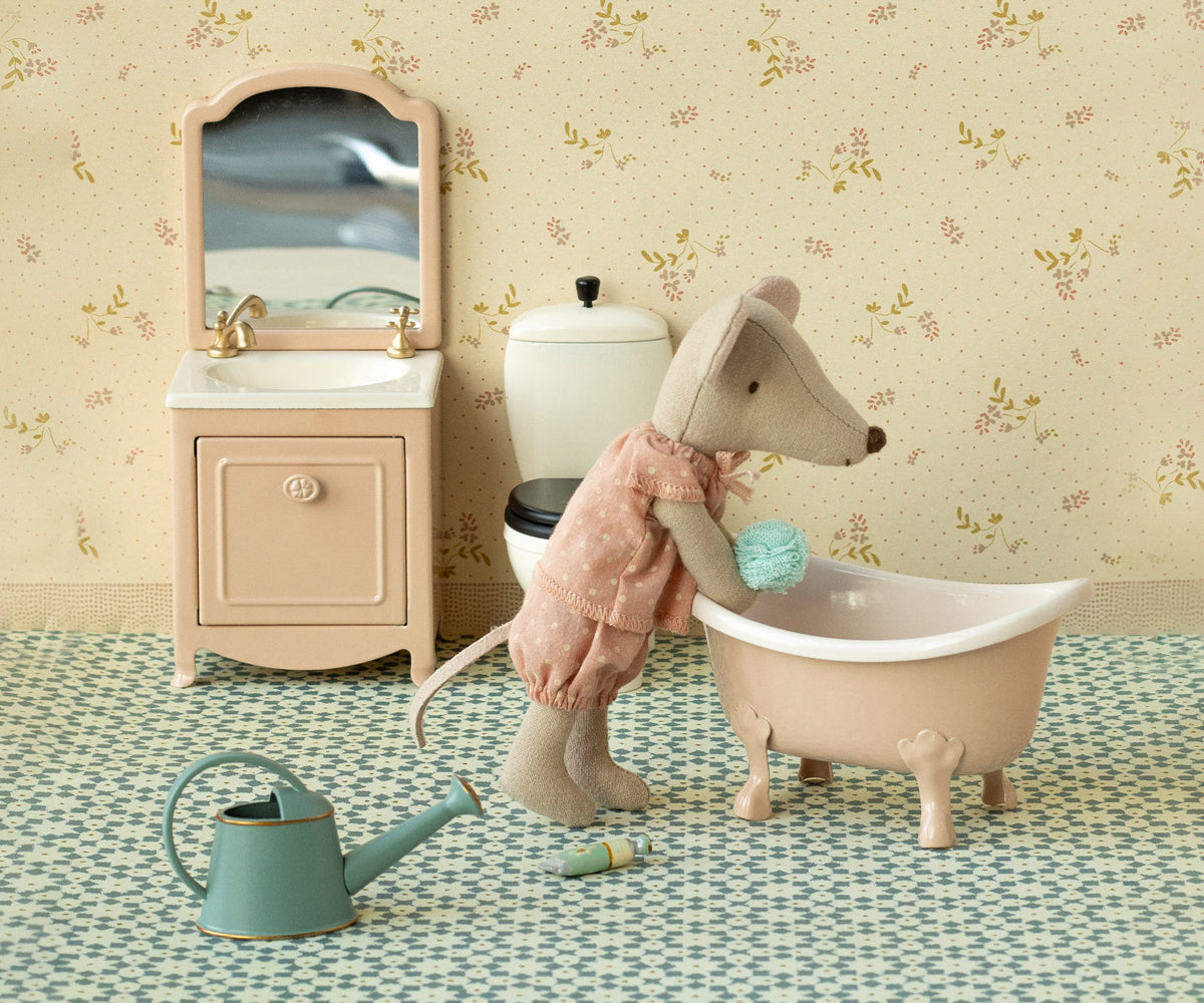 Toy mouse in a bathtub with bathroom furniture and decor in the background.