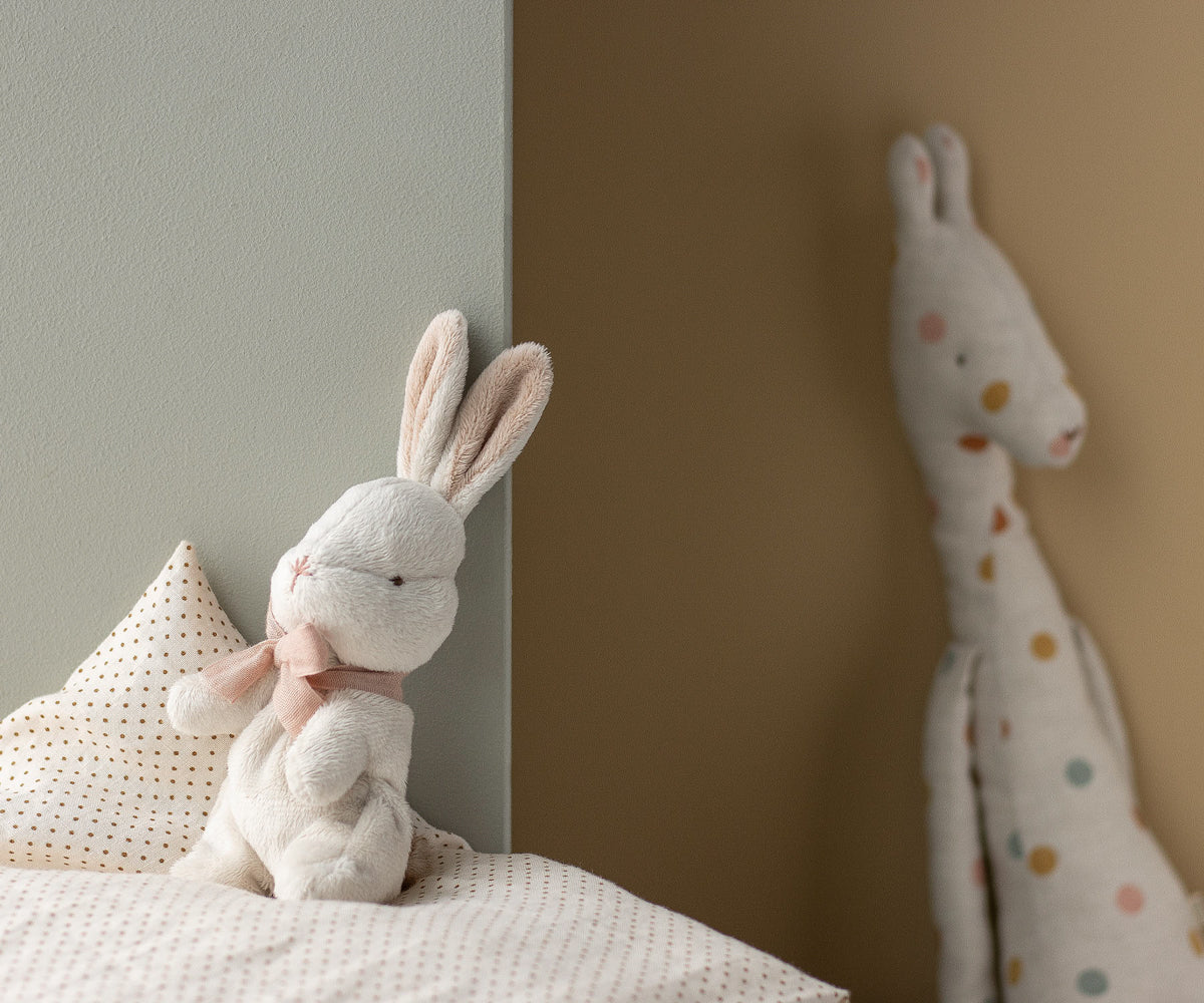 Stuffed rabbit toy on a bed with a neutral wall background.