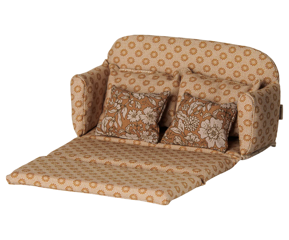 A compact fold-out miniature sofa bed with a beige and brown floral patterned fabric, featuring two matching decorative pillows, shown on a plain white background.