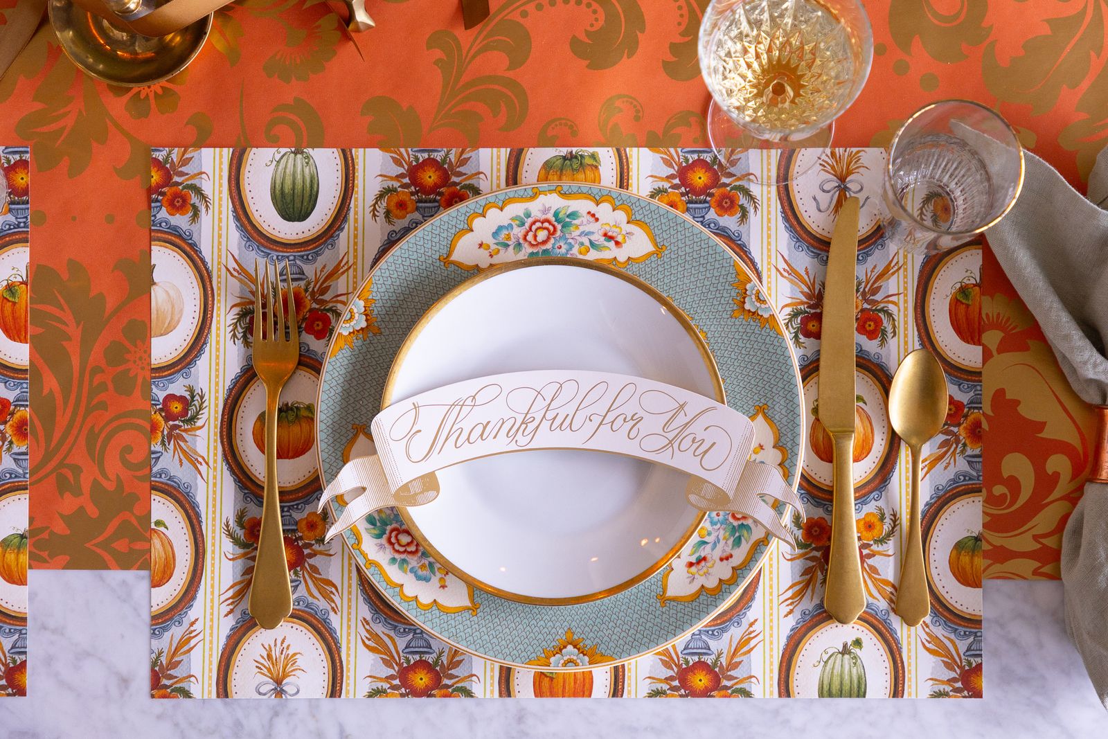 Thanksgiving table setting with decorative plates, cutlery, and a colorful placemat.