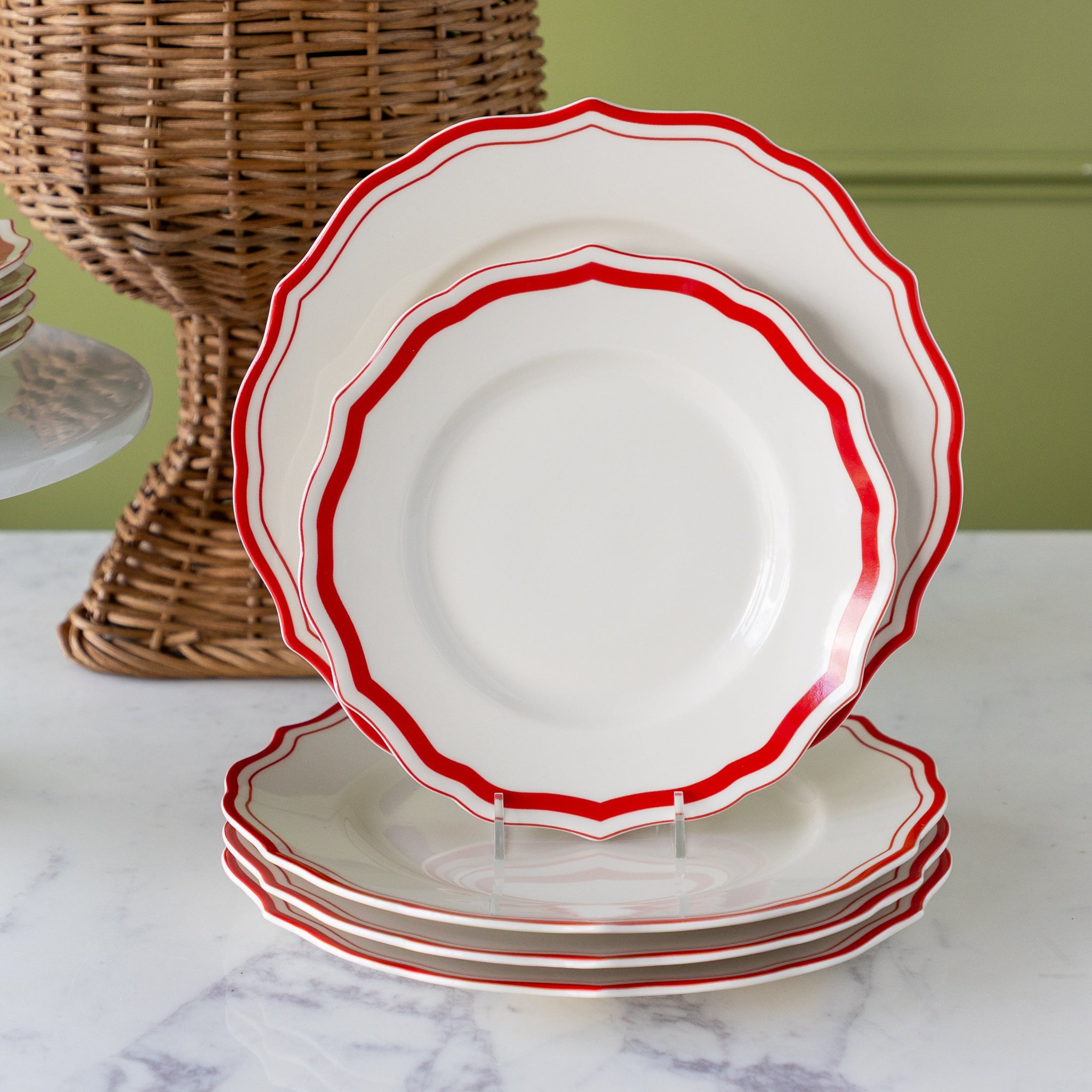 Set of white plates with red rims on a marble surface with a wicker basket in the background.