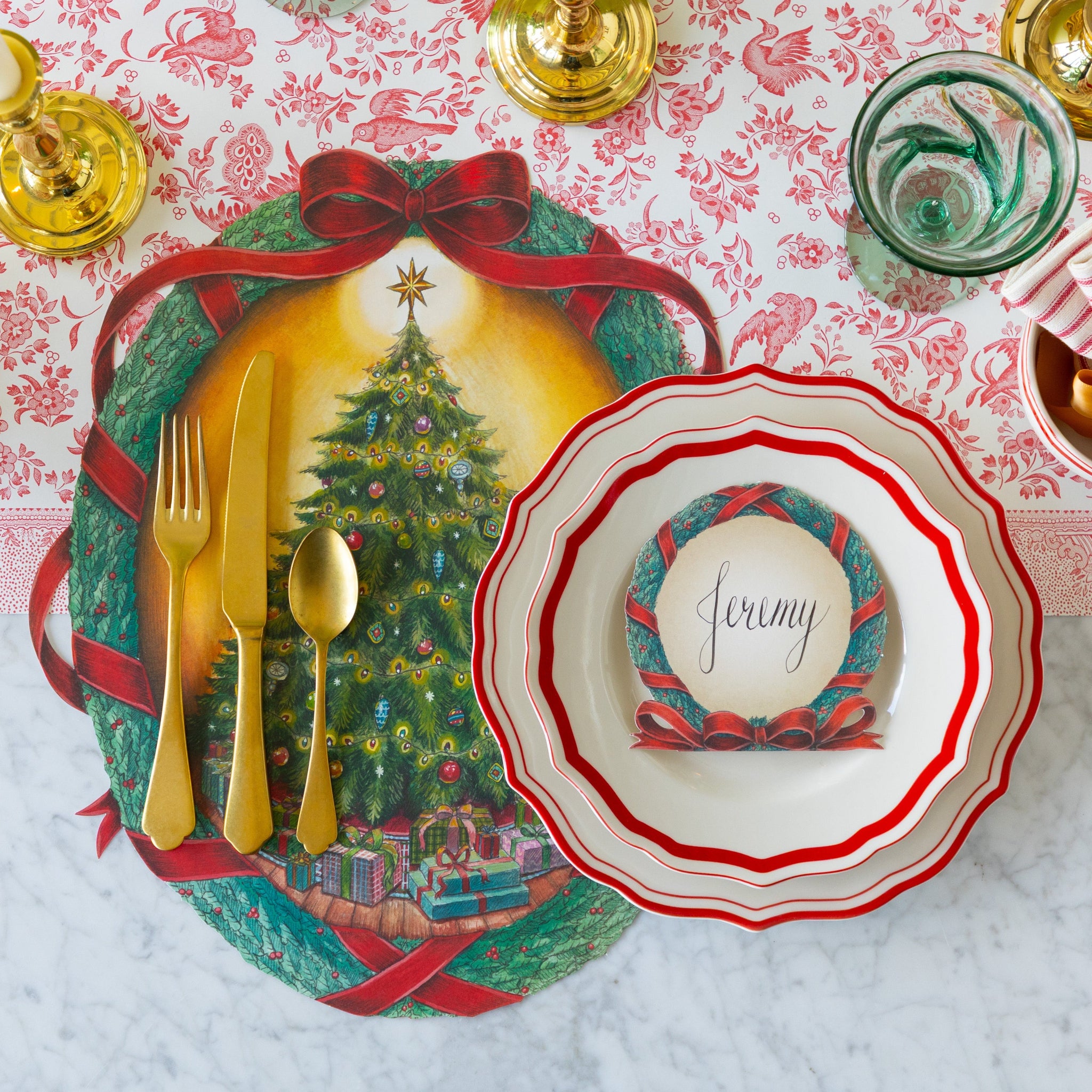 Christmas-themed table setting with red icing on the cake plates, gold cutlery, and candles on the O Christmas Tree Placemat and Red Regal Peacock Runner.