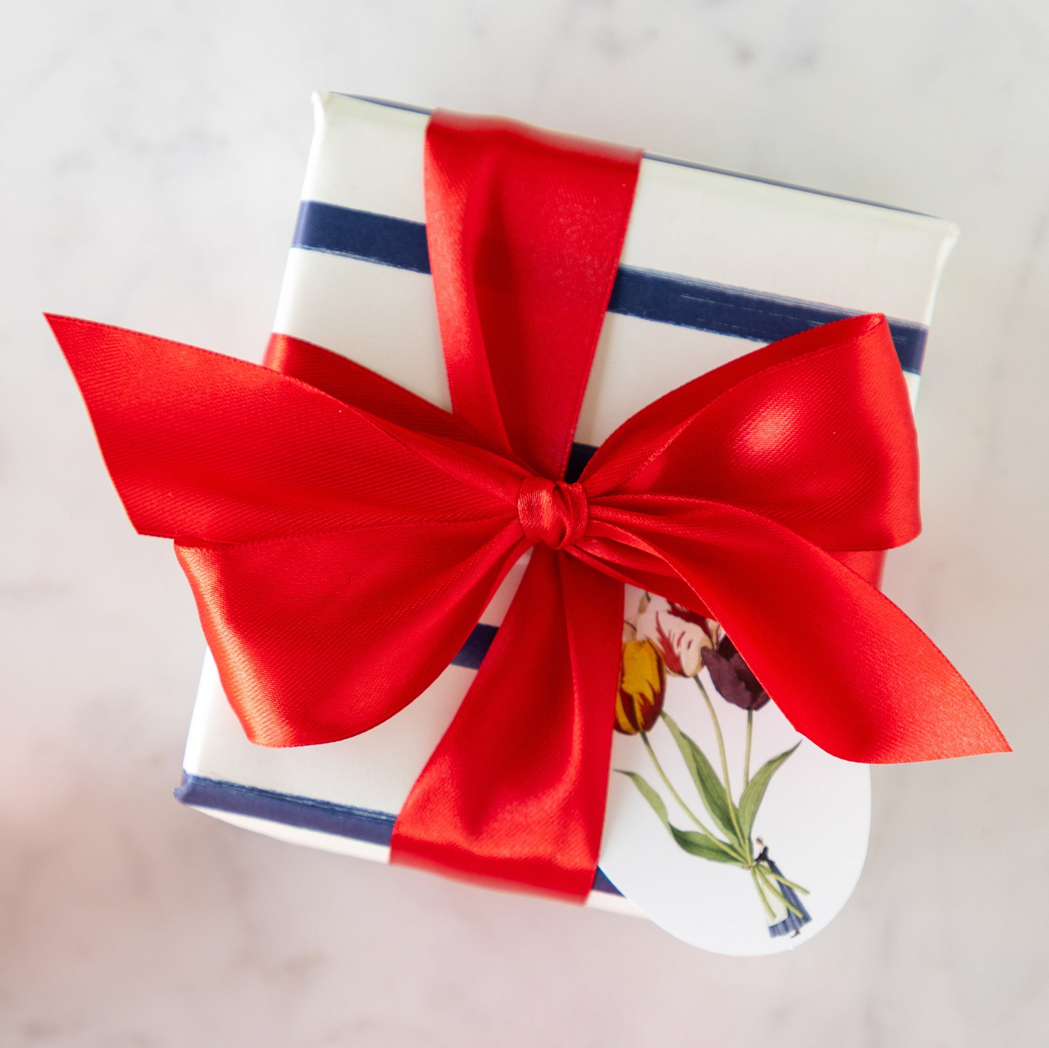 A present wrapped in a bow with the Fancy Red Ribbon featuring a Laura Stoddart gift tag.