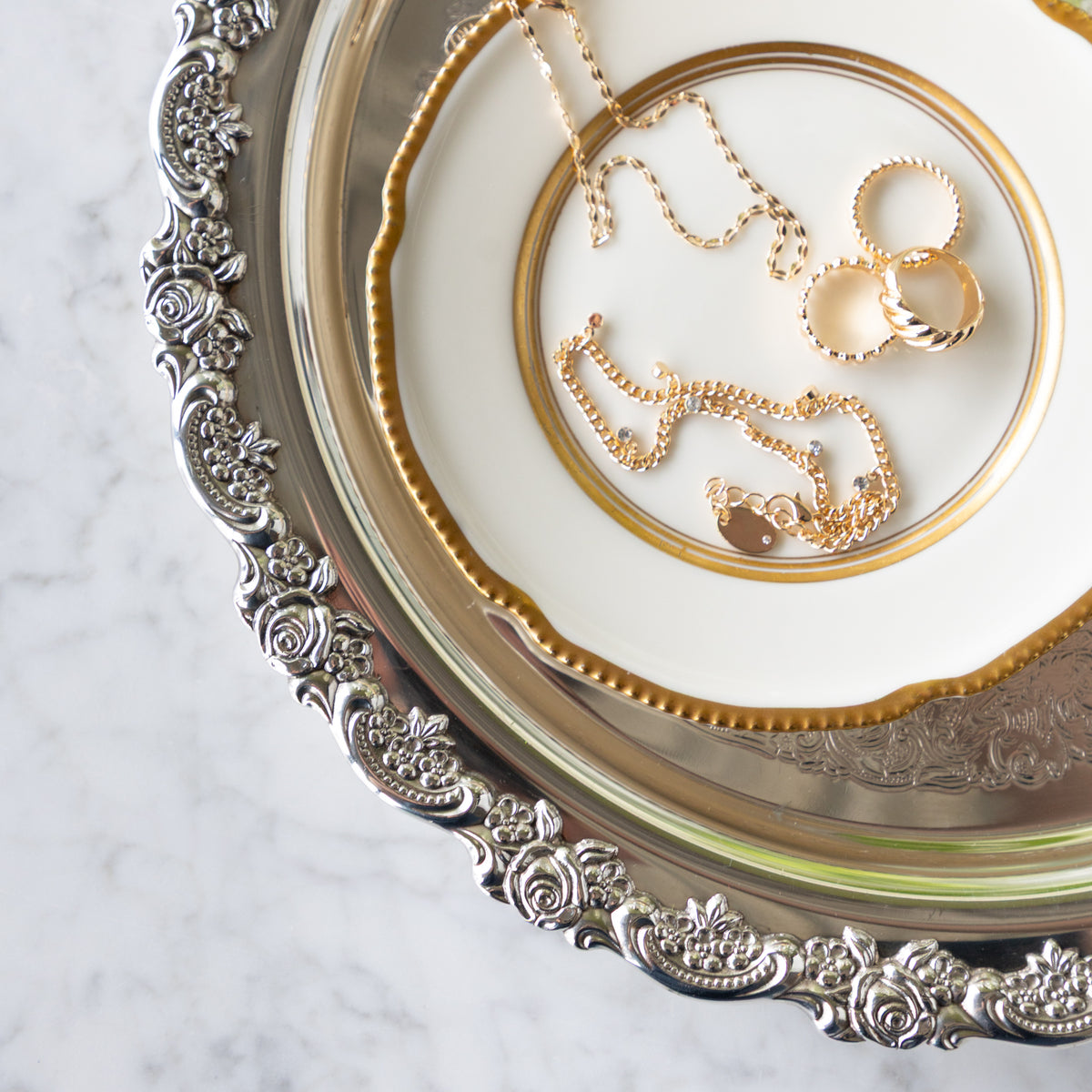 Gold jewelry on a decorative silver platter with a marble background.