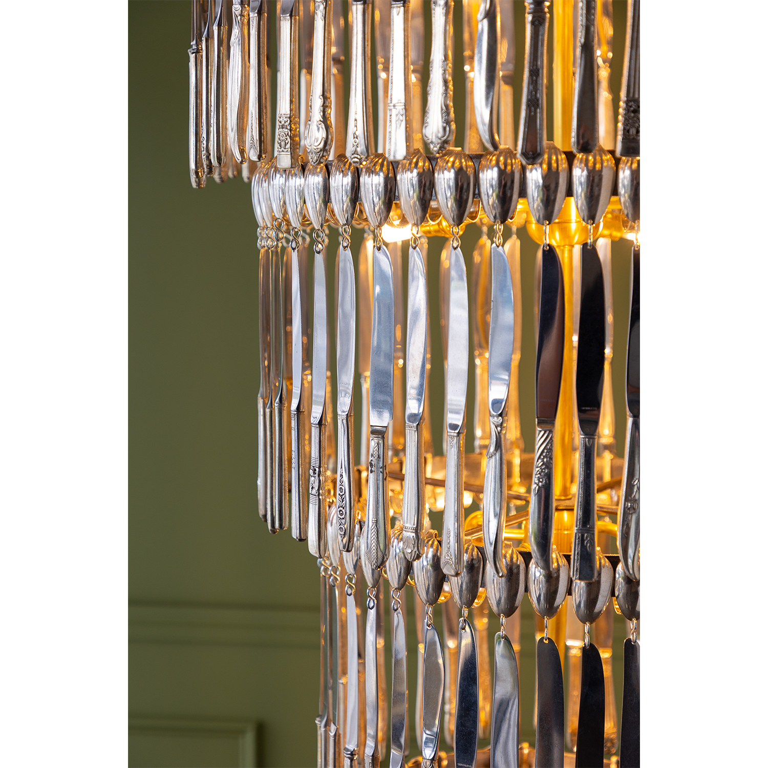 A close-up of a modern chandelier featuring hanging silver-toned metal pieces with engraved floral details, illuminated by warm yellow lights from behind.