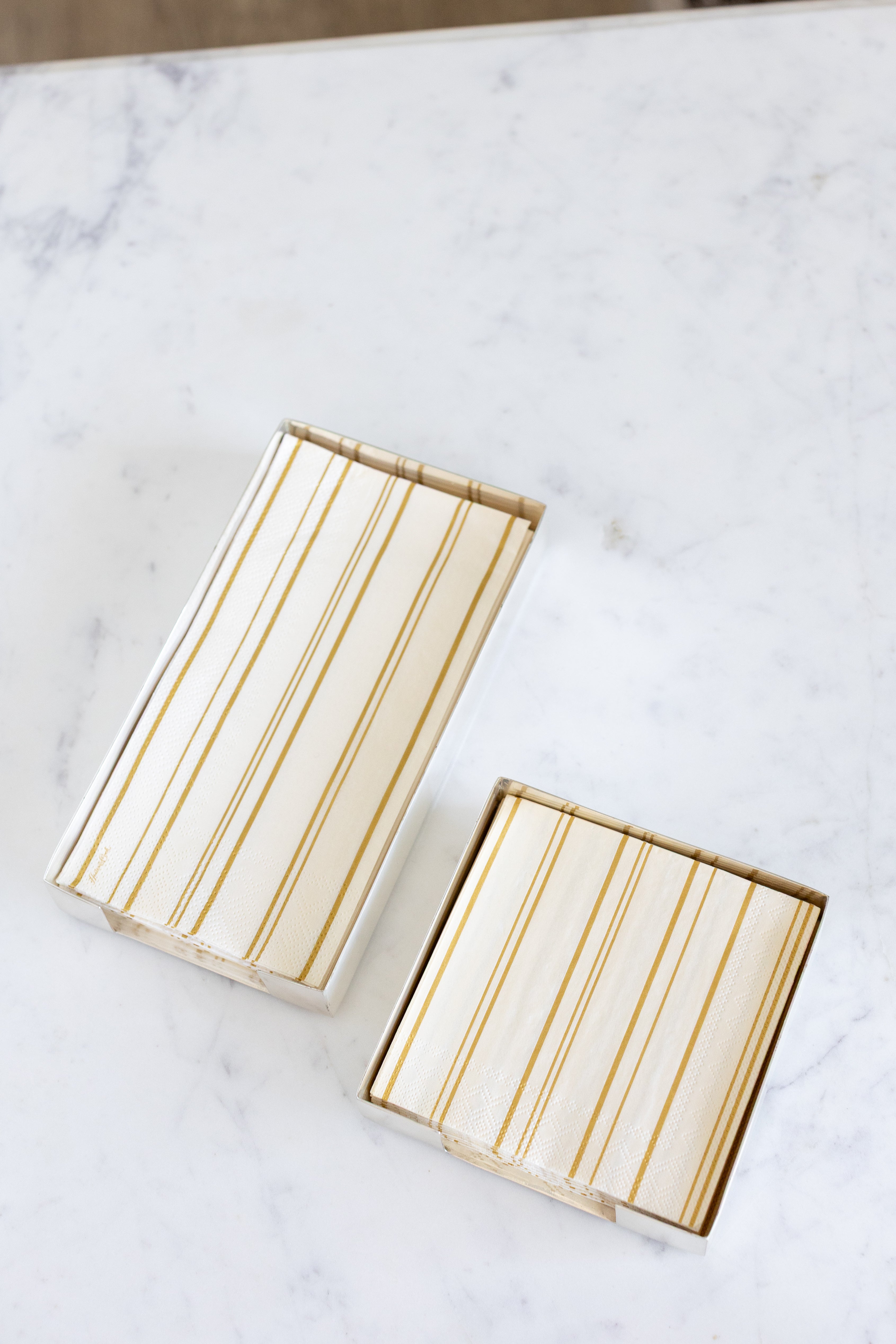 Two Silver Napkin Holders, guest-sized and cocktail-sized, containing napkins on a white table.