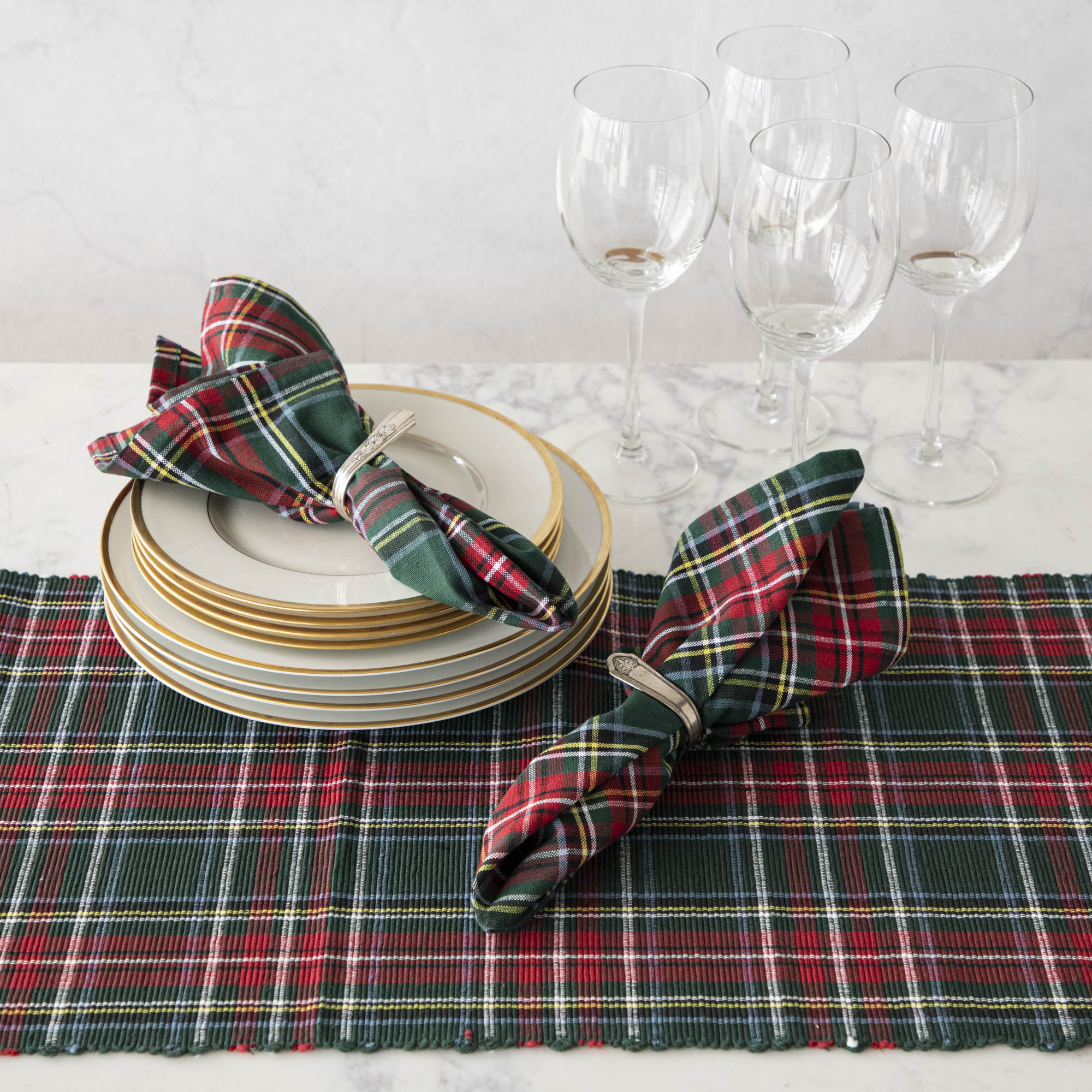 Two green and red plaid cotton napkins in napkin rings, on a table set with a matching plaid runner.