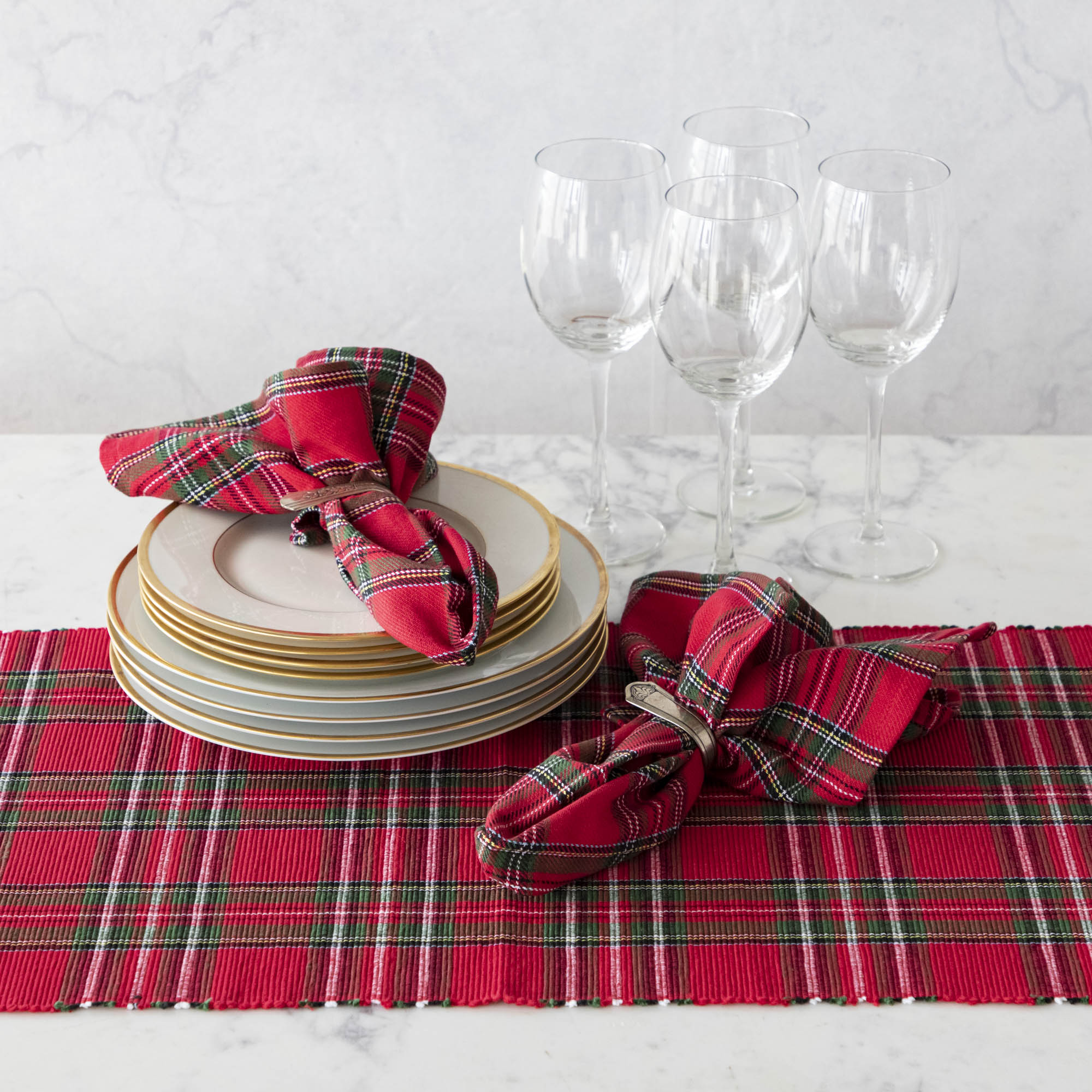 Two red plaid cotton napkins in napkin rings, on a table set with a matching plaid runner.