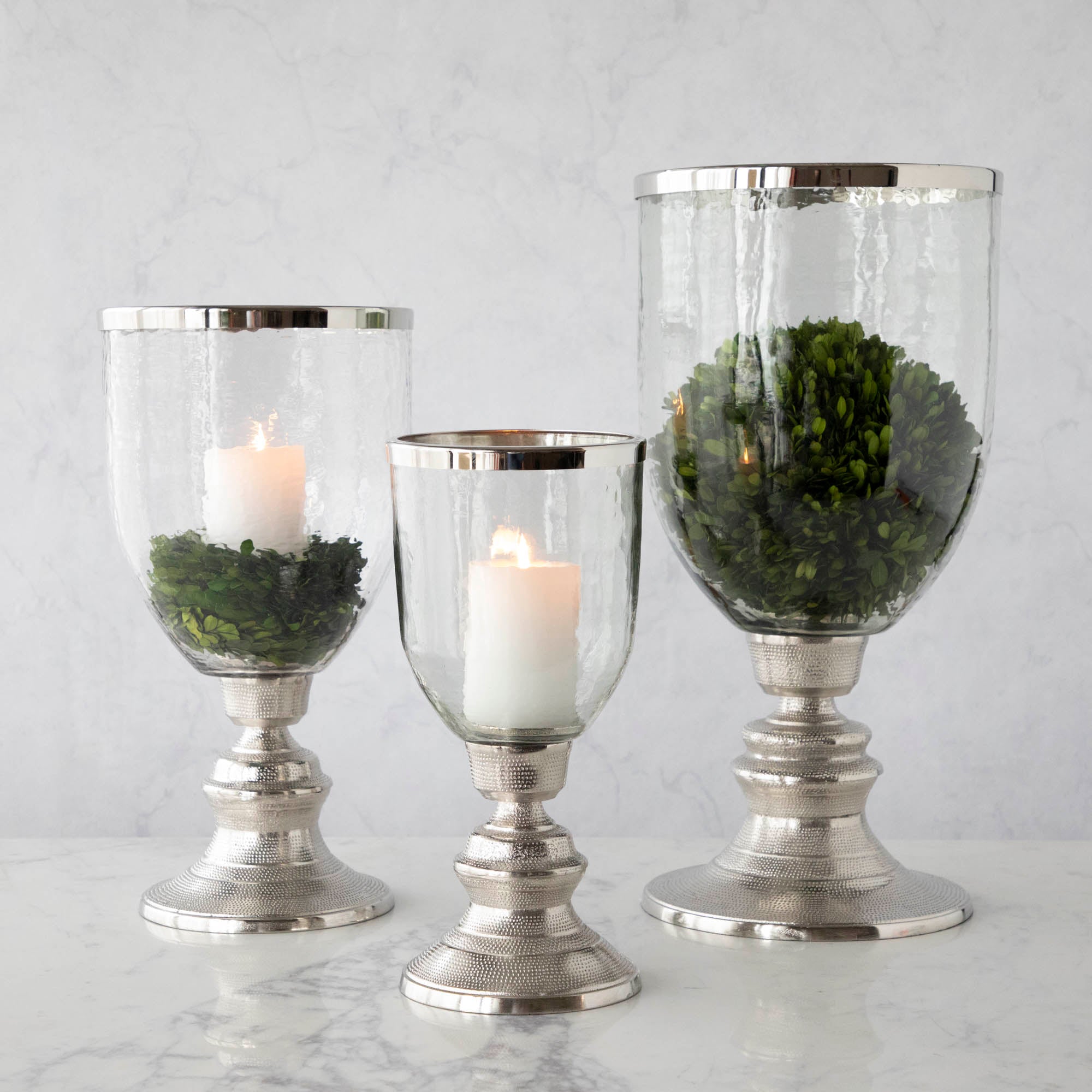 A small, medium and large Candle Hurricane Holder filled with a candle and boxwood.