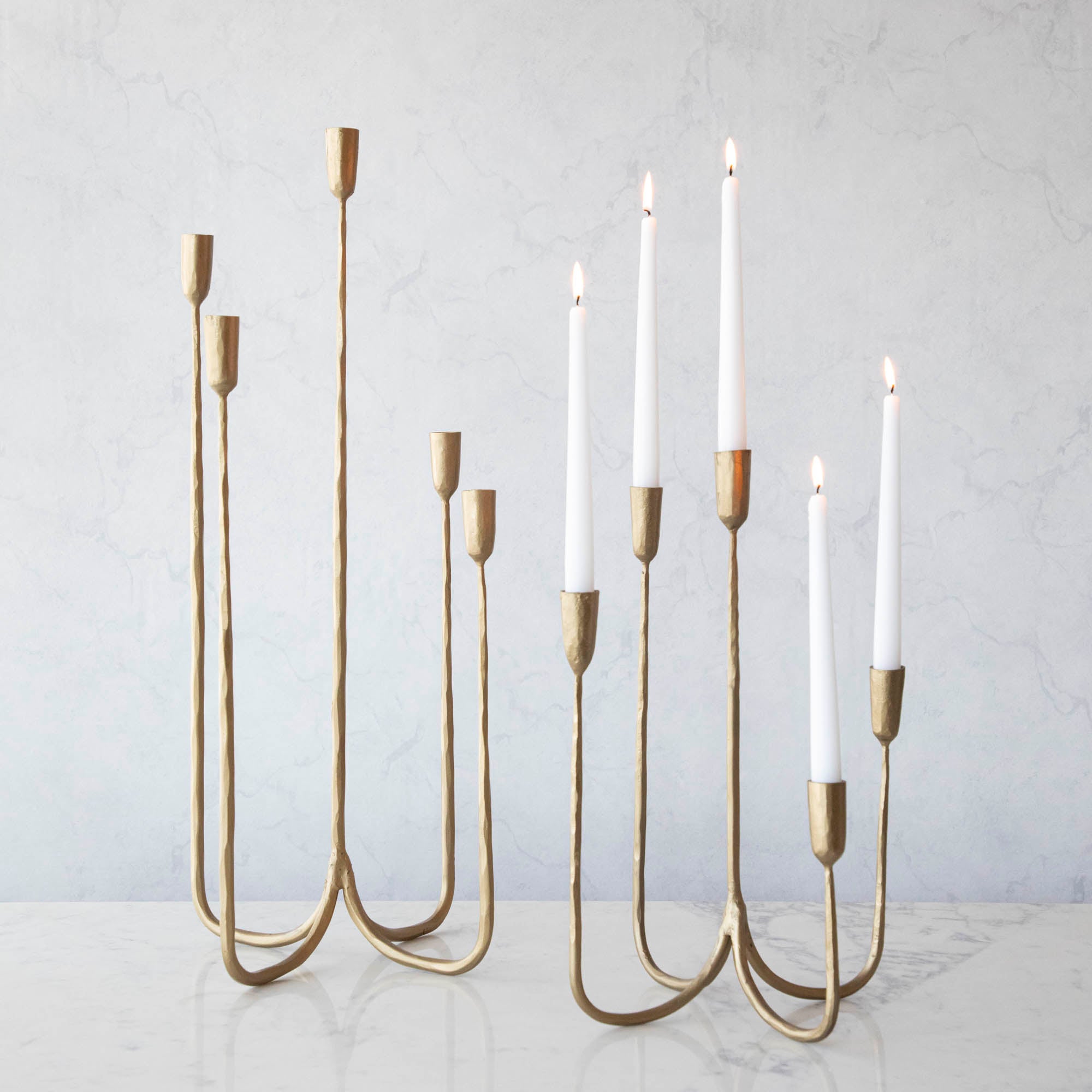 Forged Brass Candelabra in short and tall sizes with white candles lit in them.