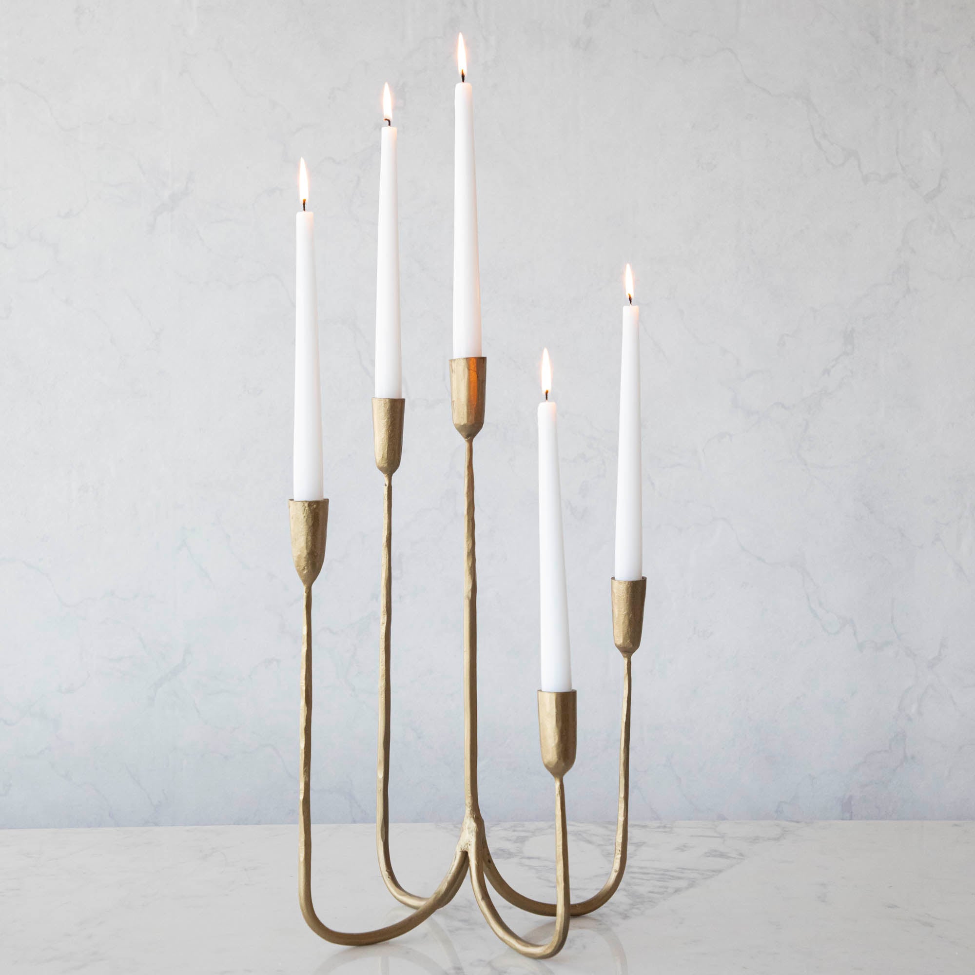 Tall Brass Forged Candelabra with white candles burning in it.