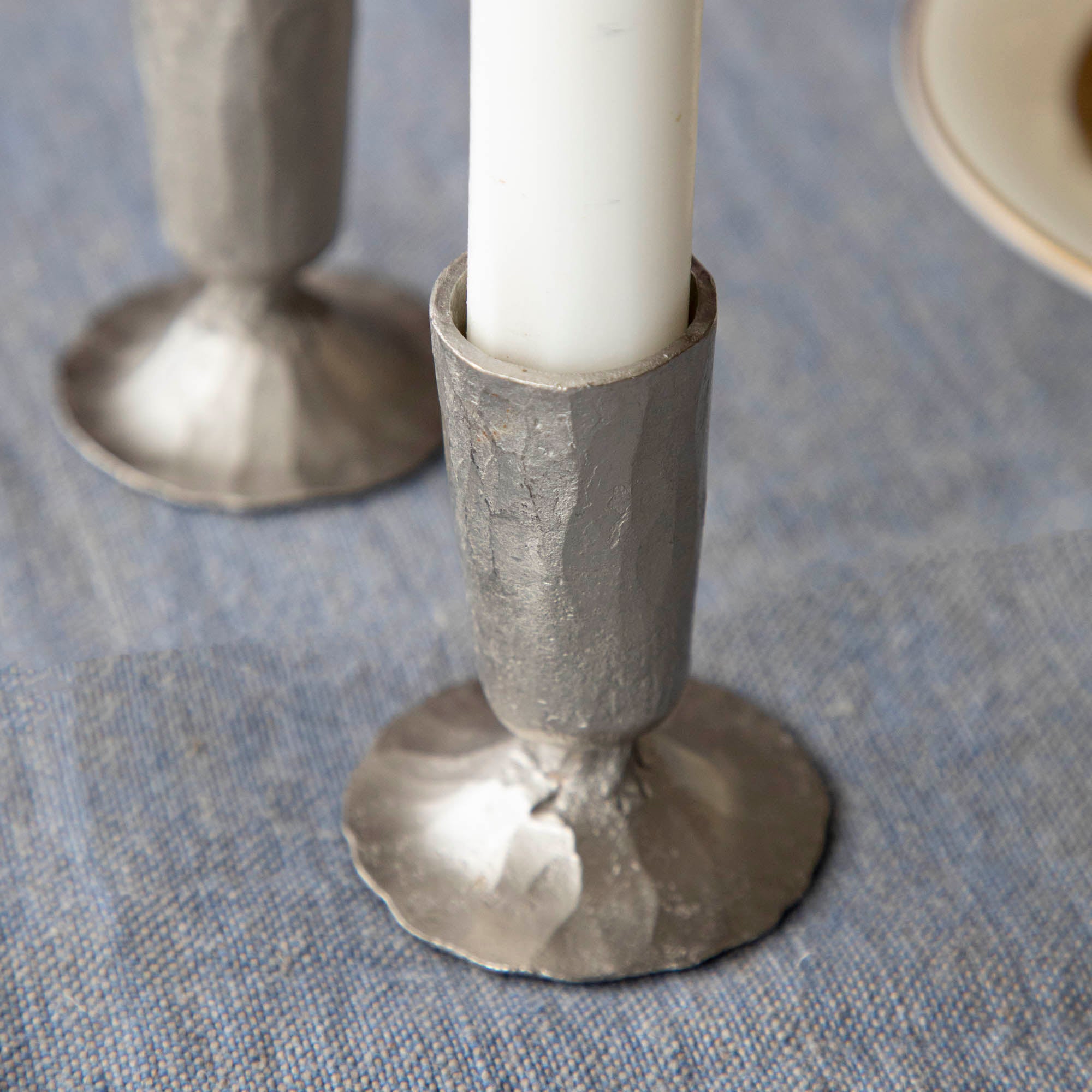 Two nickel Creative Co-Op metal taper holders holding candles on a table.