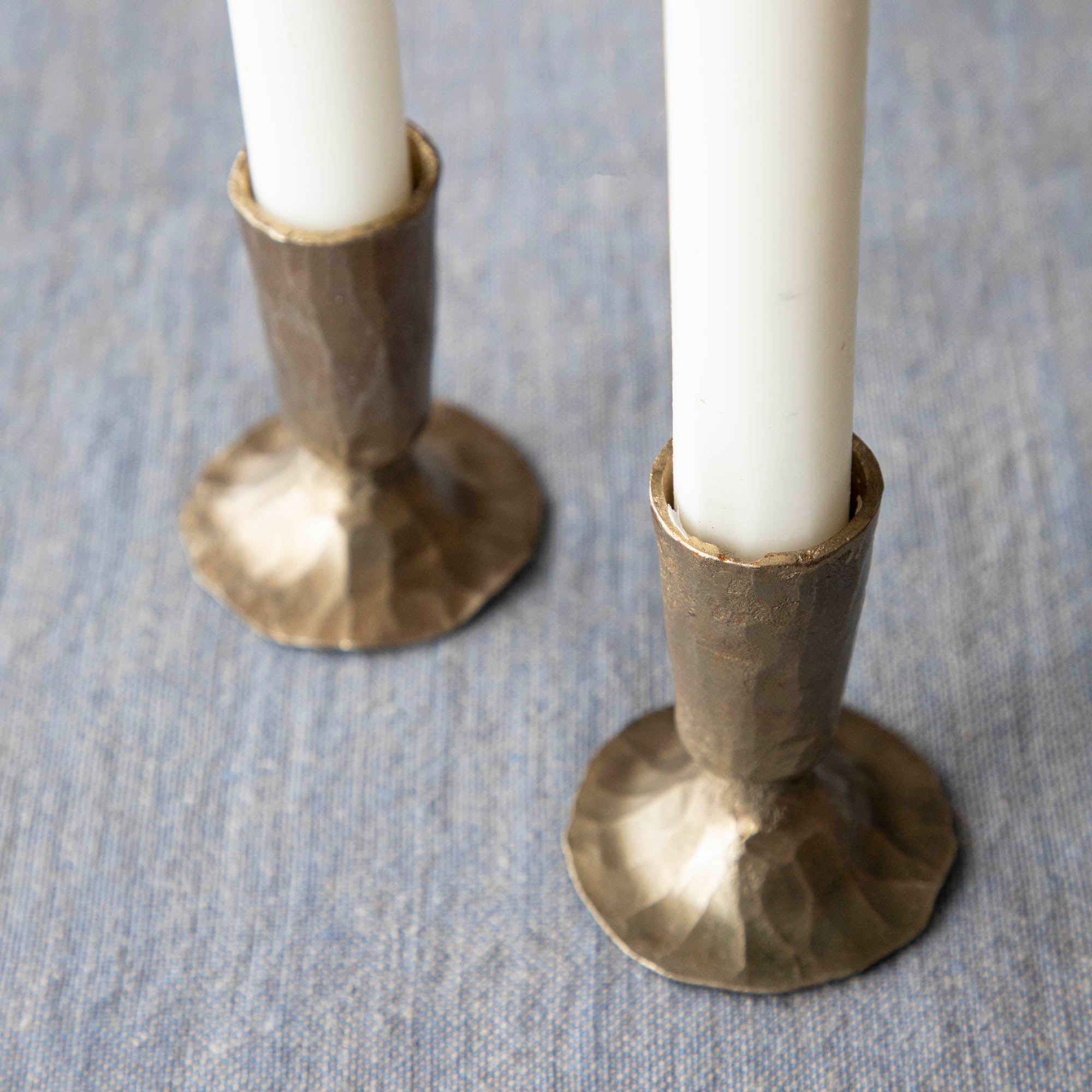 Two bronze Creative Co-Op metal taper holders holding candles on a table.