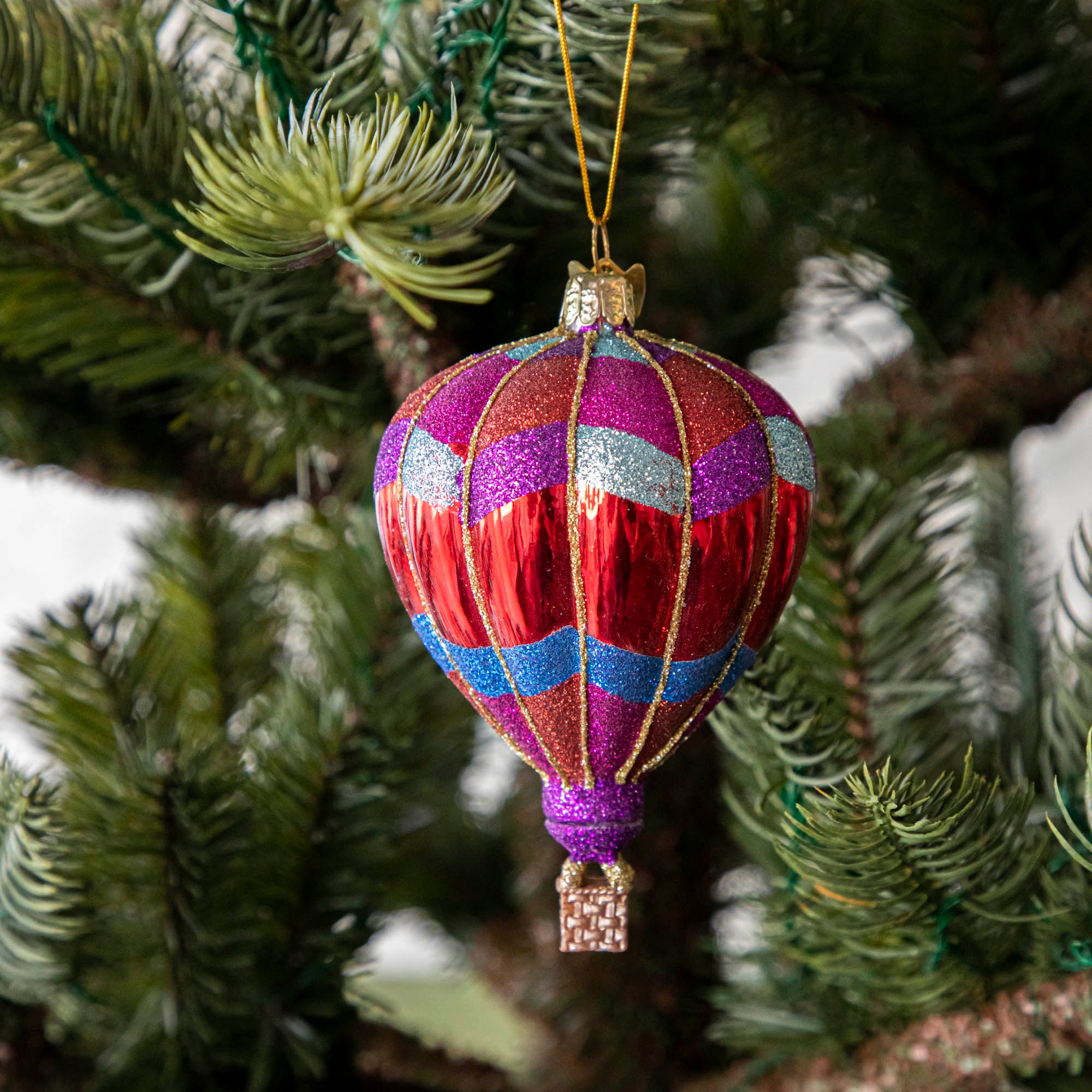 A glass hot air balloon ornament in red, blue, and purple stripes, hanging on a Christmas tree.