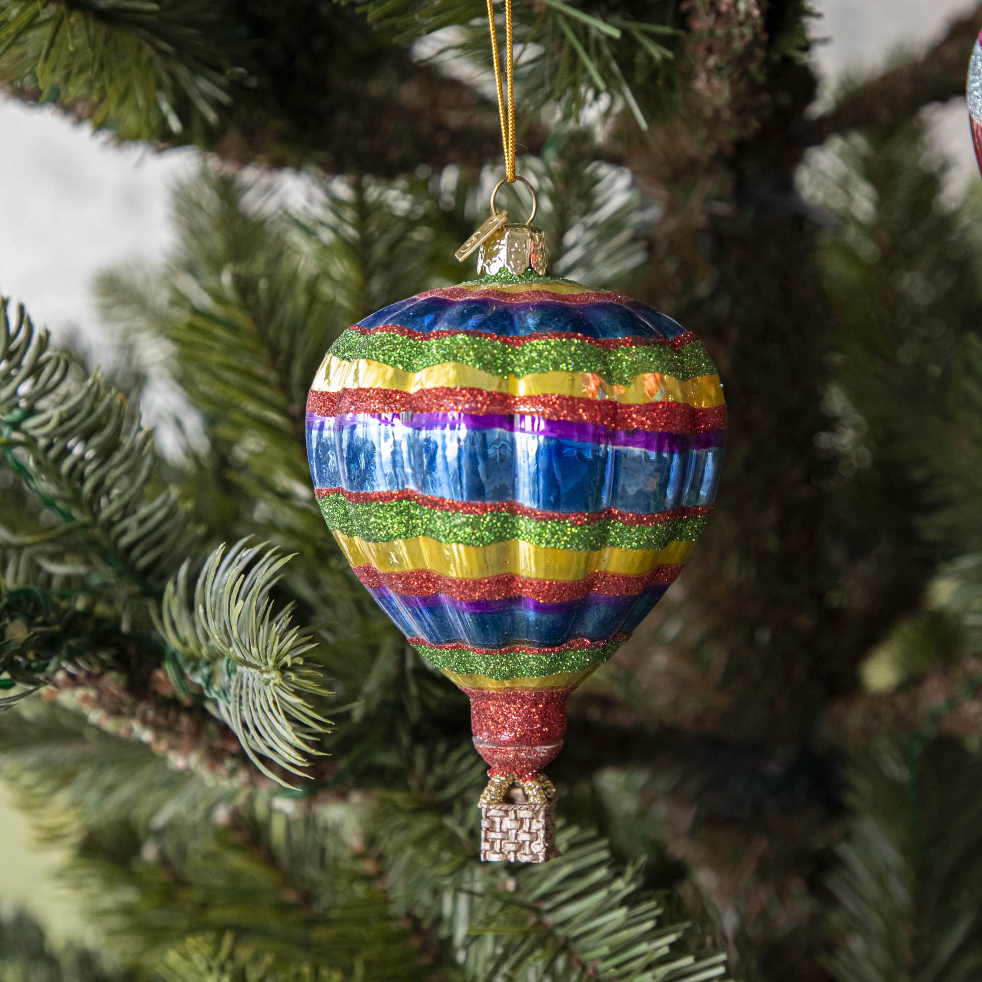 A glass hot air balloon ornament in red, blue, green, and yellow stripes, hanging on a Christmas tree.