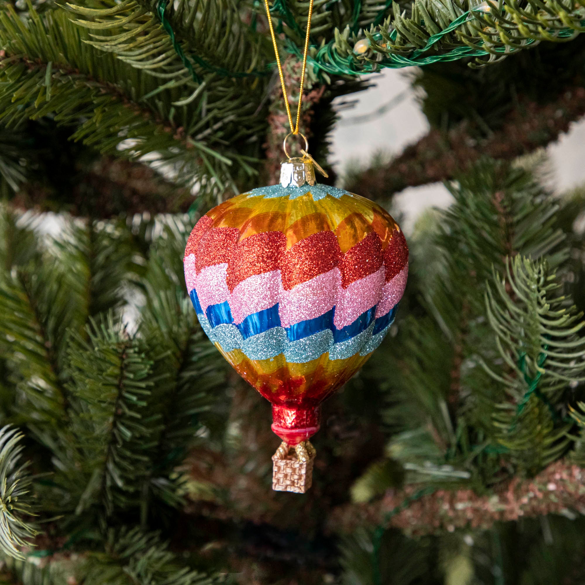 A glass hot air balloon ornament in red, pink, blue, yellow, orange and red stripes, hanging on a Christmas tree.