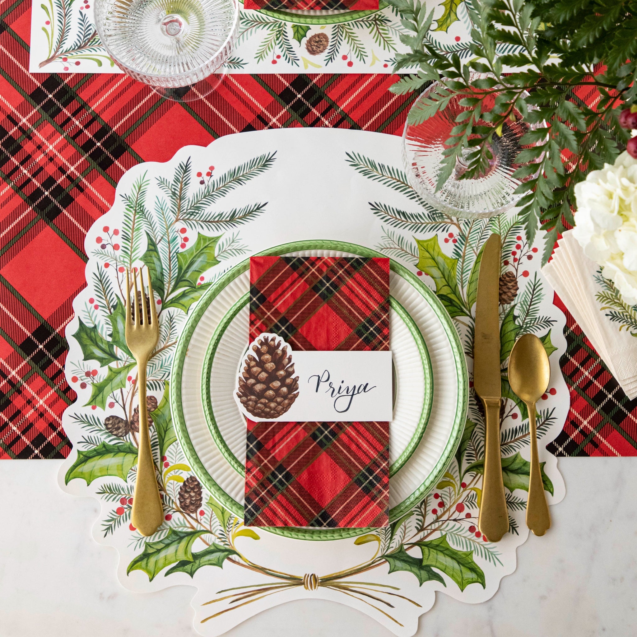 Christmas-themed table setting with the Die-cut Christmas Sprigs Placemat, Red Plaid Napkin, Pinecone Place Card and gold cutlery on the Red Plaid Runner.