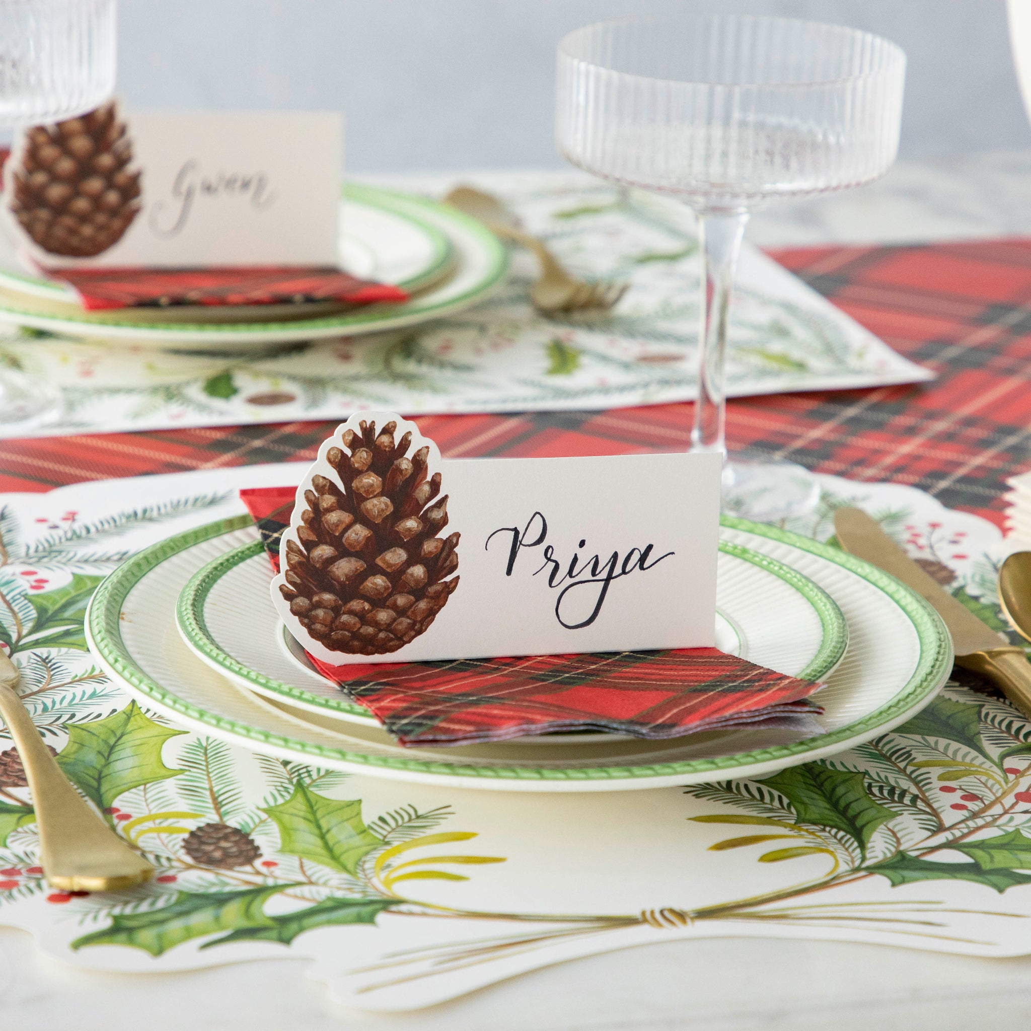 The Pinecone Place Card atop a place setting with the Die-cut Christmas Sprigs, Red Plaid Guest Napkin and Red Plaid Runner underneath.