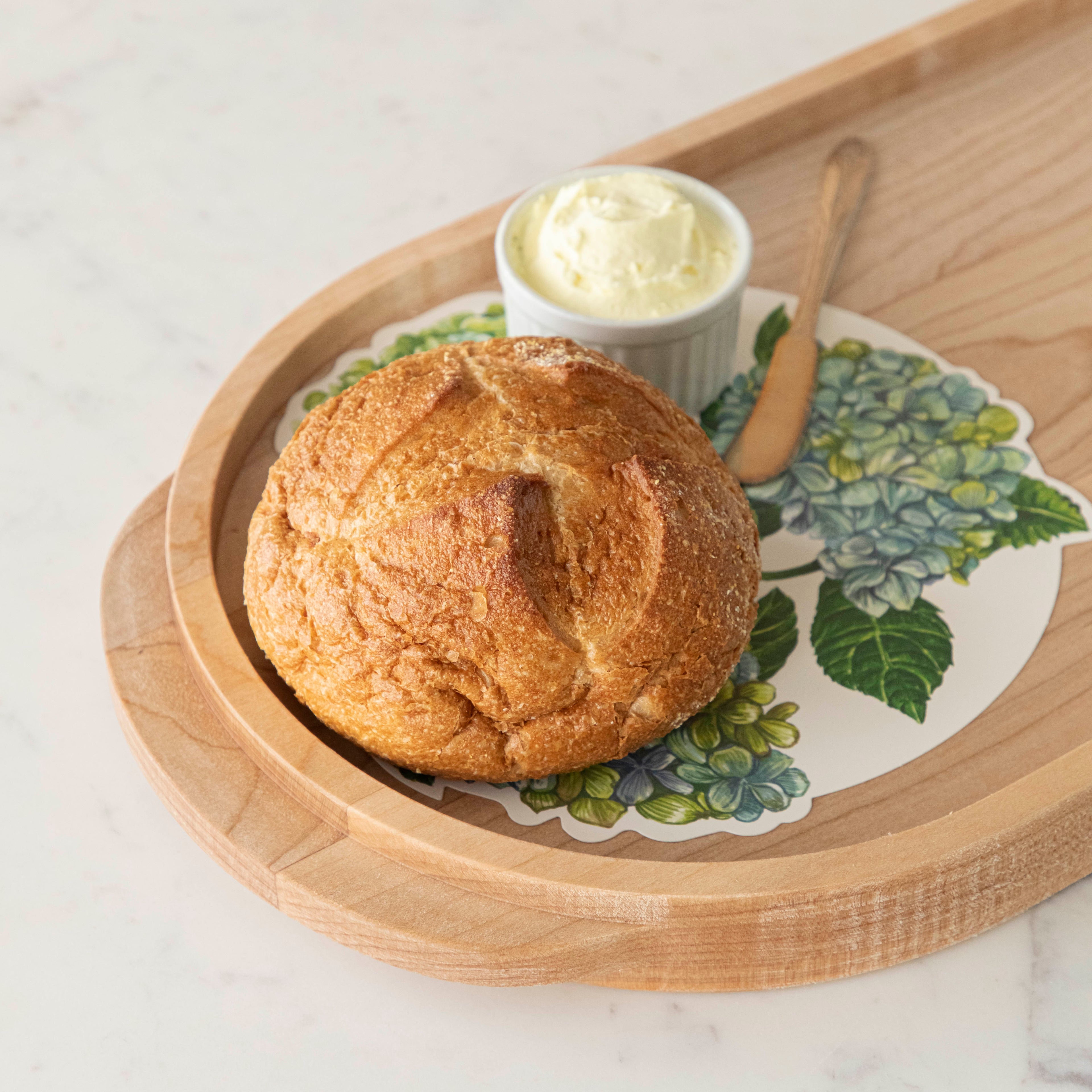 A Hydrangea Serving paper under a loaf of bread with a ramakin of butter.