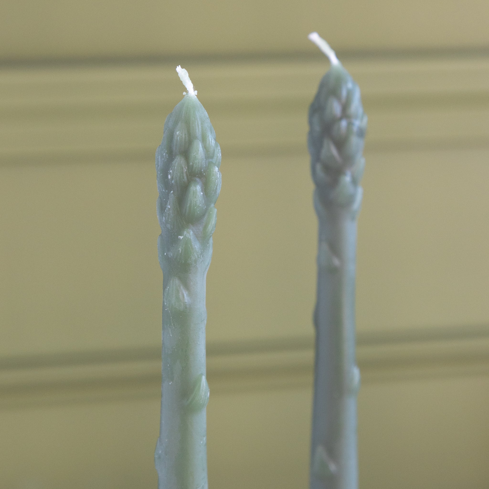 Two asparagus shaped candles on a green background.