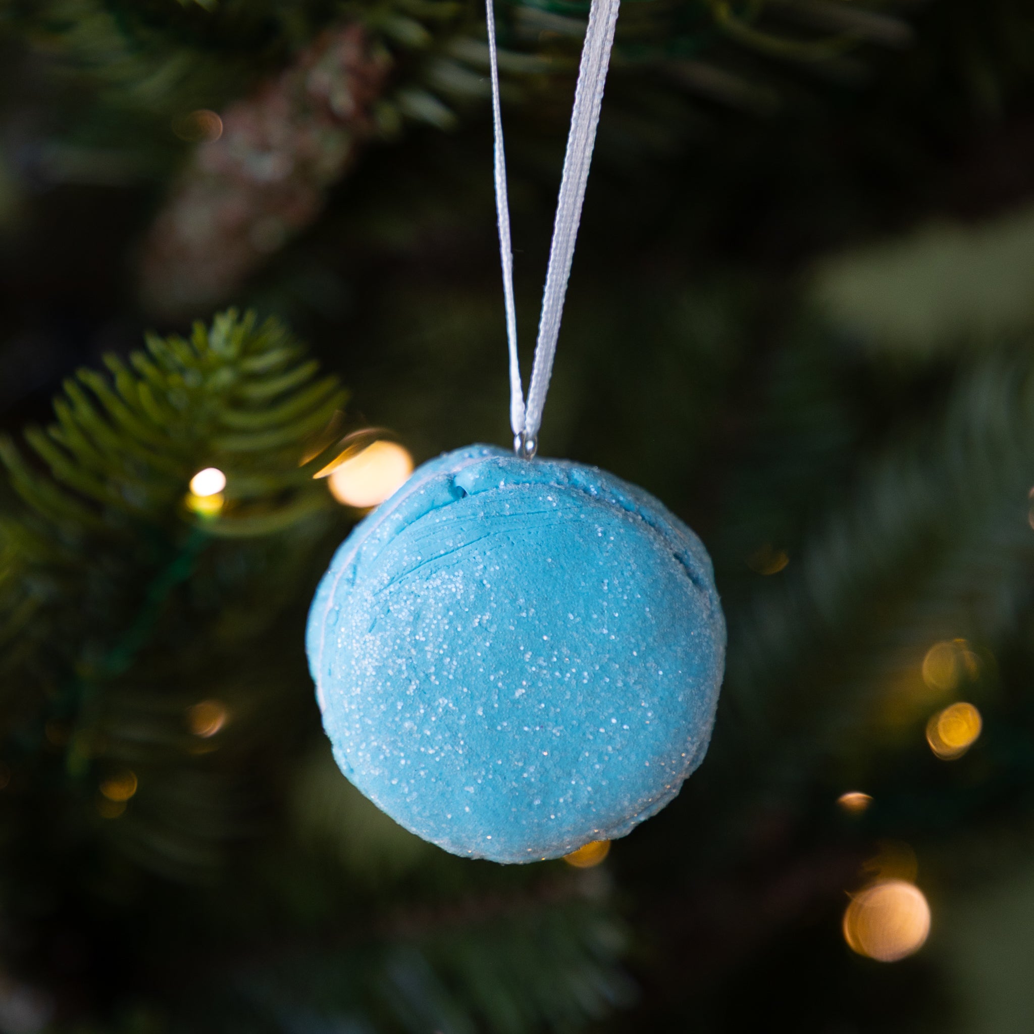 Blue macaron ornament hanging on a Christmas tree with blurred lights in the background.