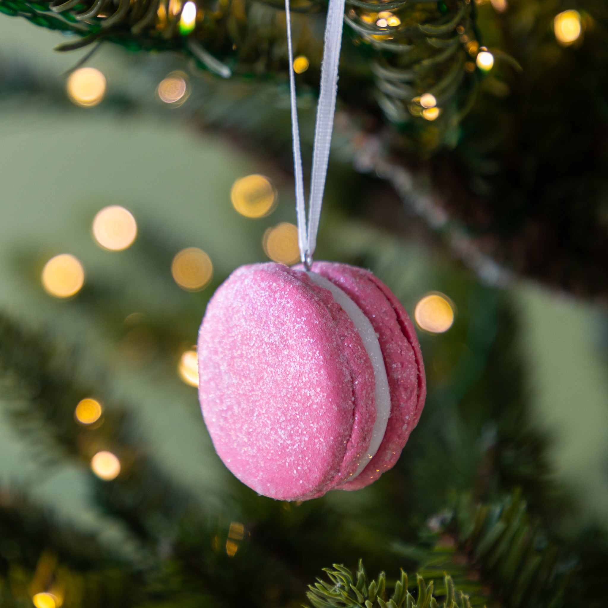 Pink macaron ornament hanging on a Christmas tree with blurred lights in the background.