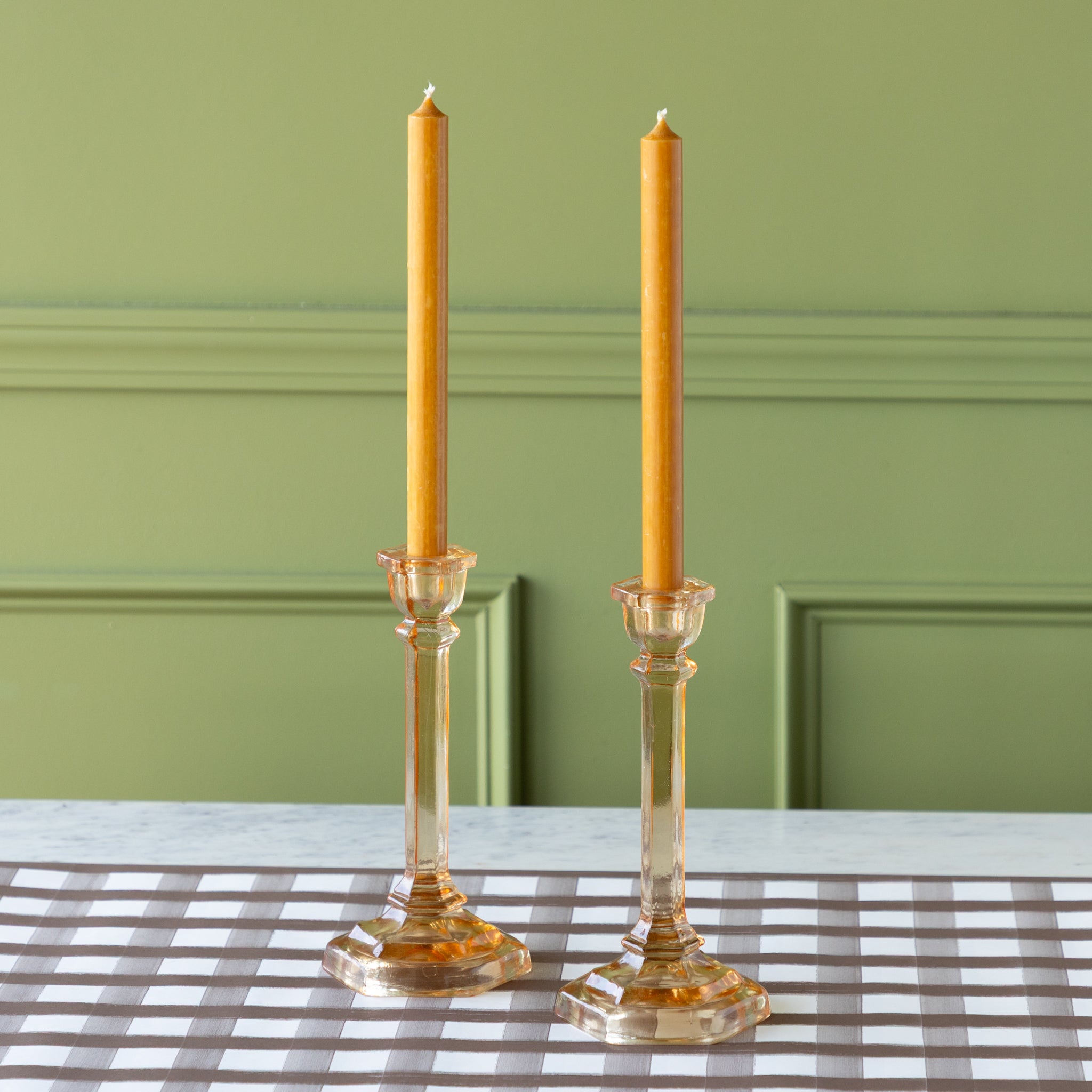 Amber Glass Taper Holders with orange taper candles on the Brown Painted Check Runner against a green wall.