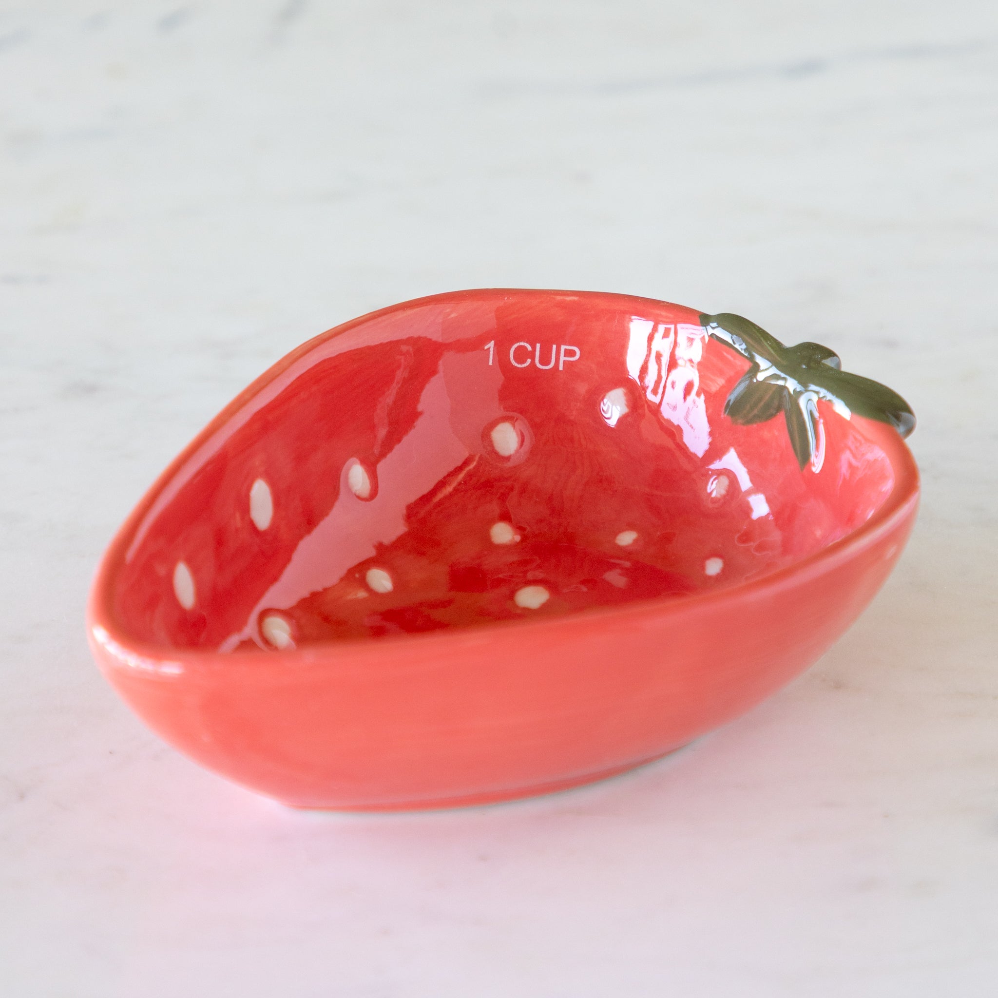 Red ceramic measuring cup shaped like a strawberry with &