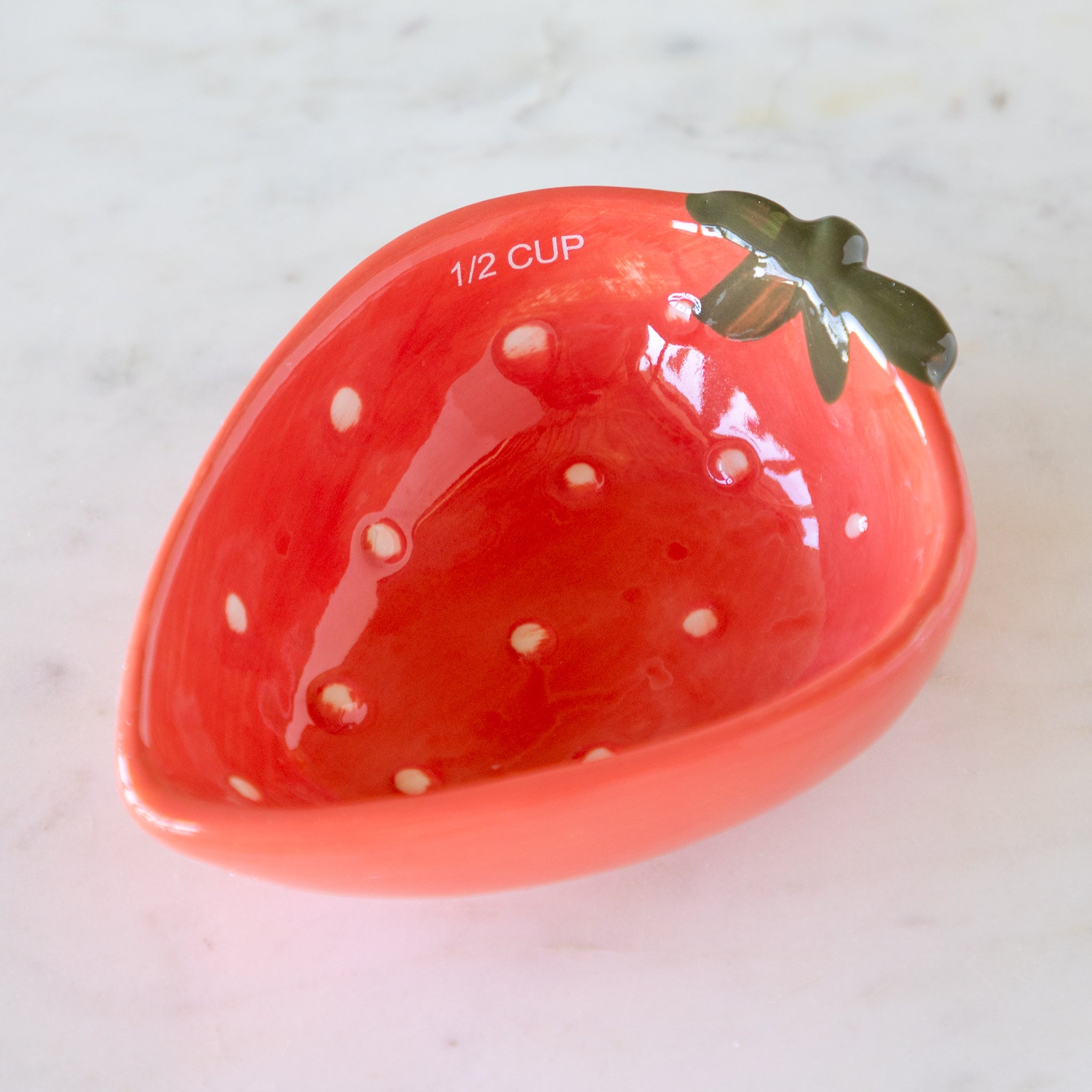 Red ceramic measuring cup shaped like a strawberry with &