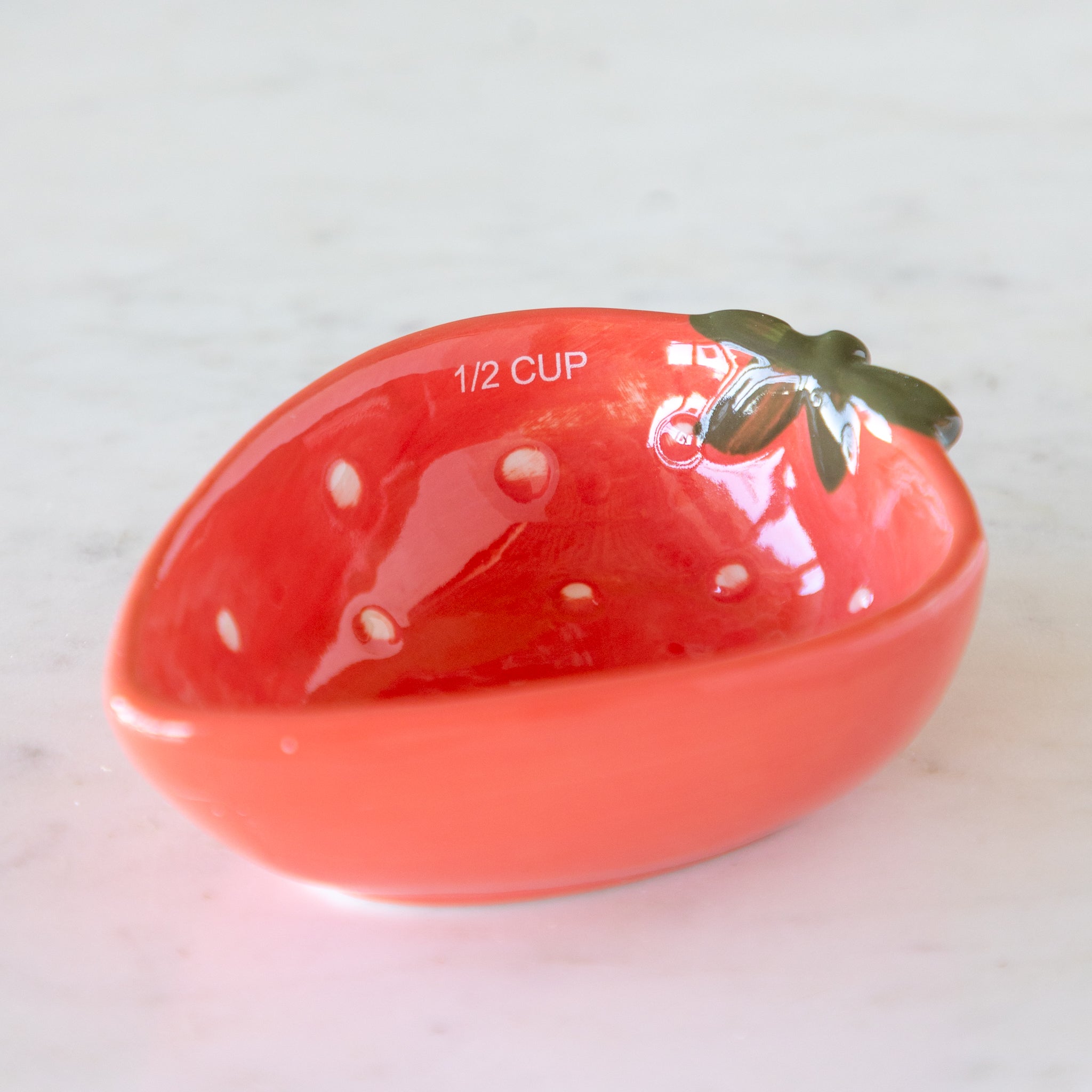 Red ceramic measuring cup shaped like a strawberry with &