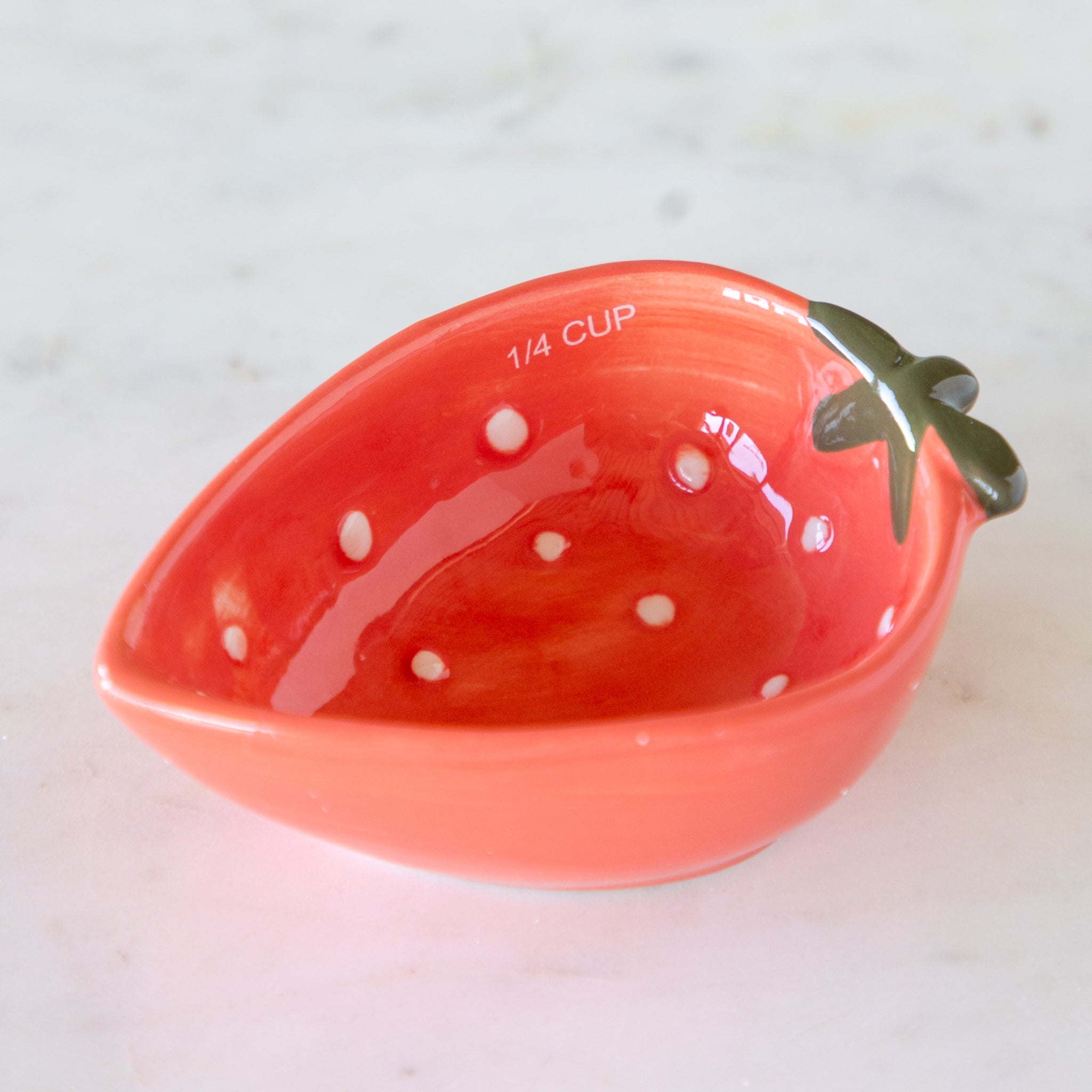 Red ceramic measuring cup shaped like a strawberry with &