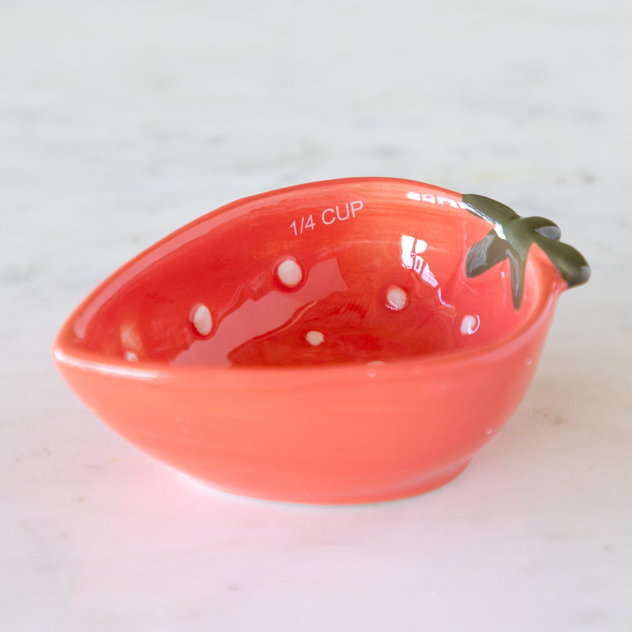 Red ceramic measuring cup shaped like a strawberry with &