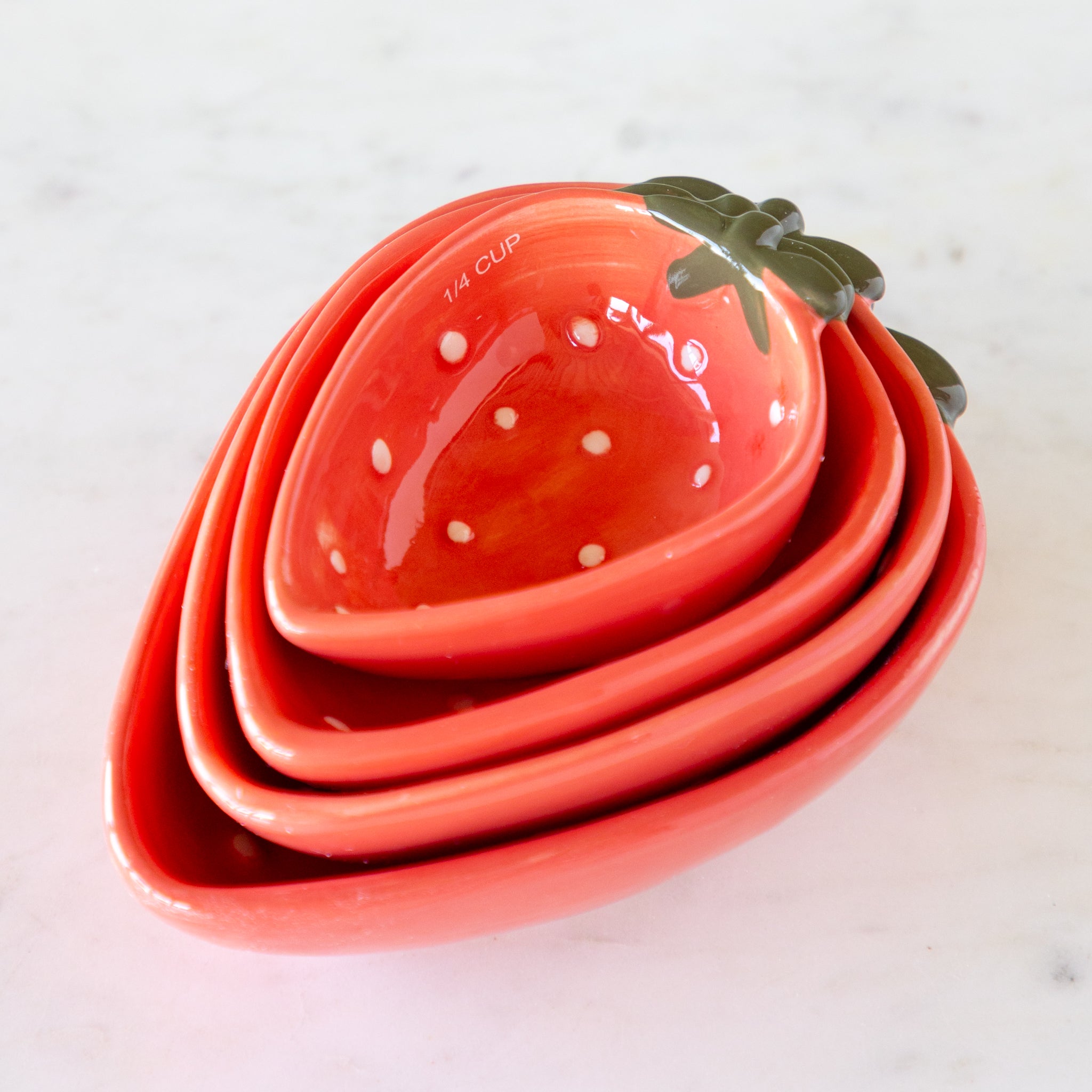 Set of strawberry-shaped measuring cups nestled together on a marble table.