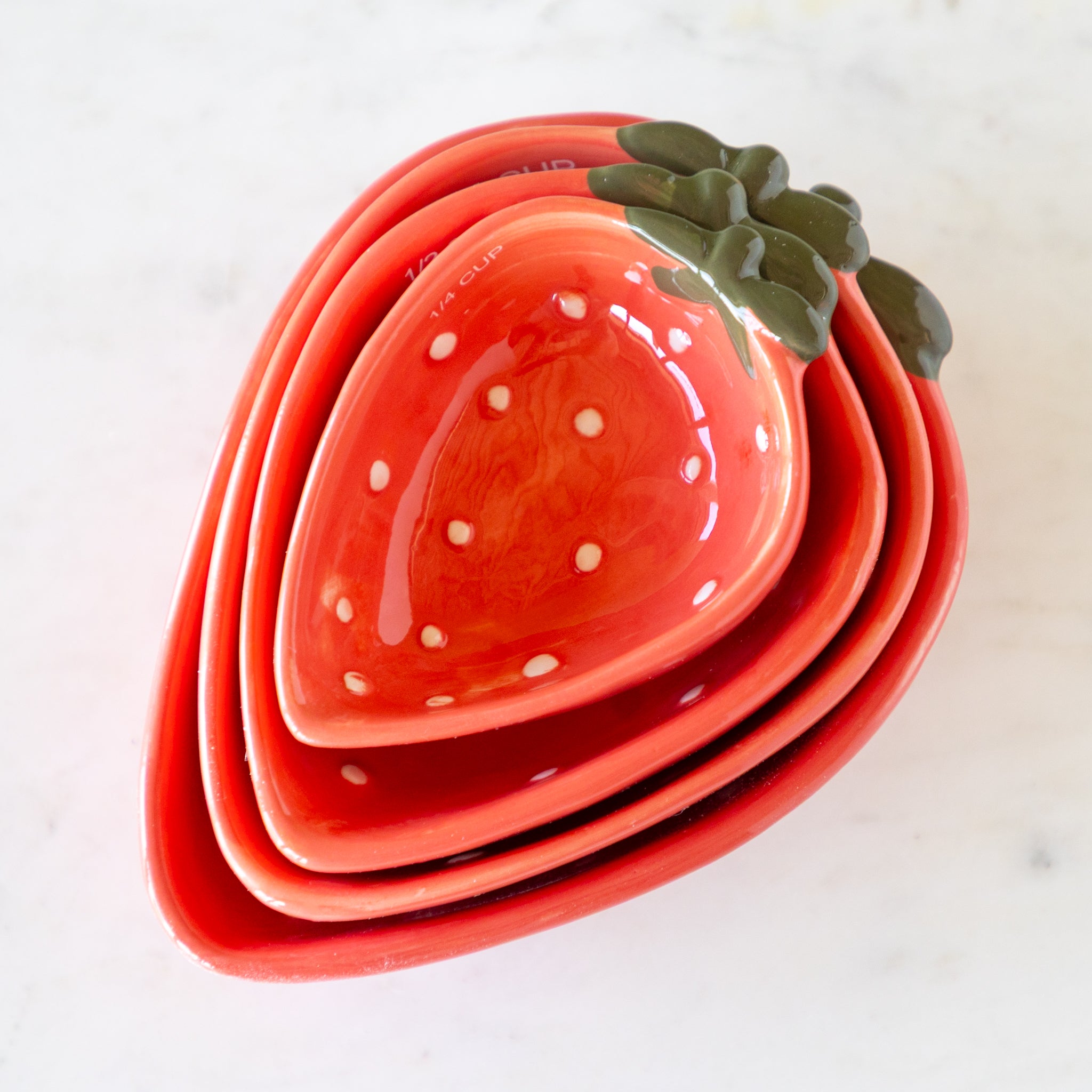Set of strawberry-shaped measuring cups nestled together on a marble table.