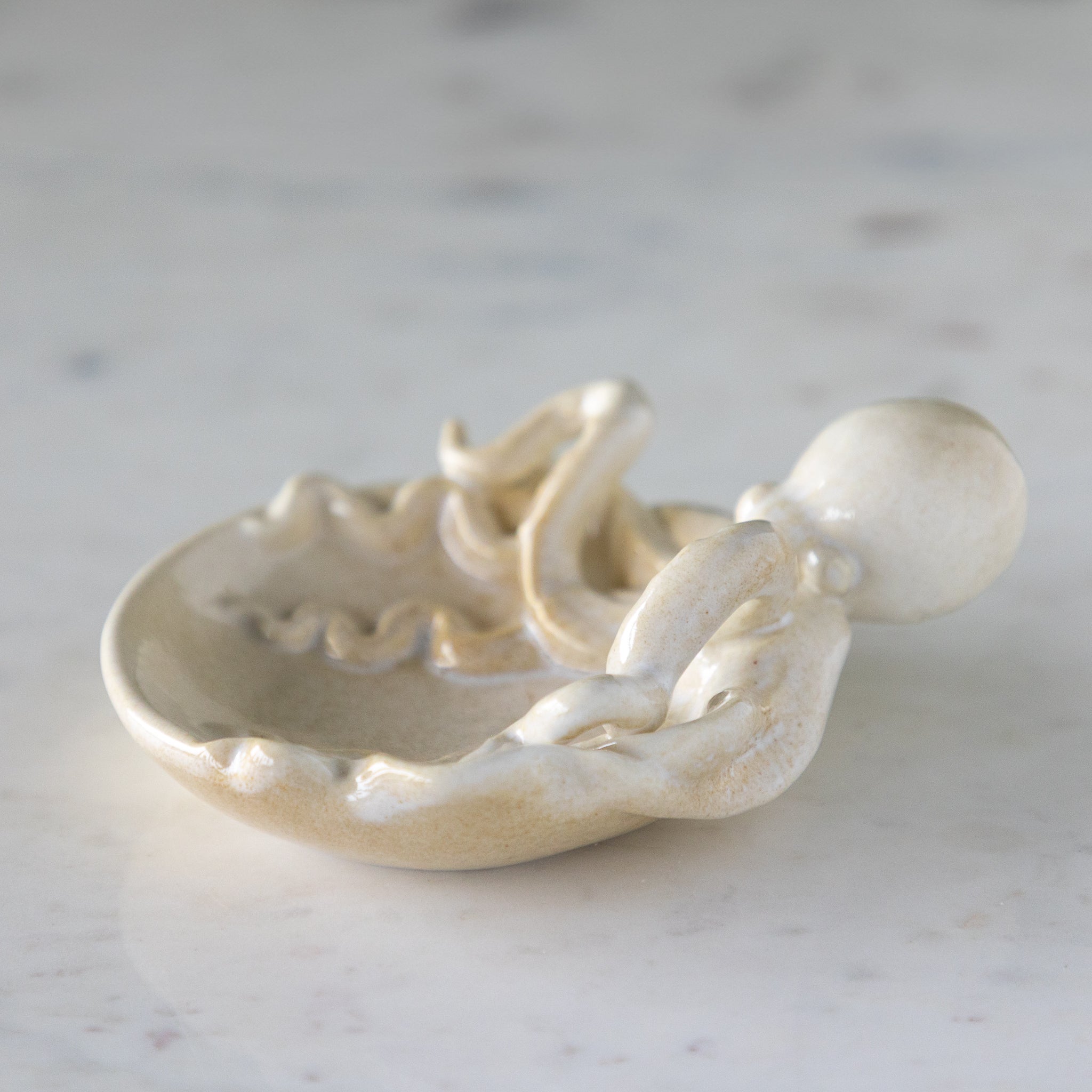 A Stoneware Octopus Dish featuring an octopus with its tentacles around a circular dish, on a marble table.